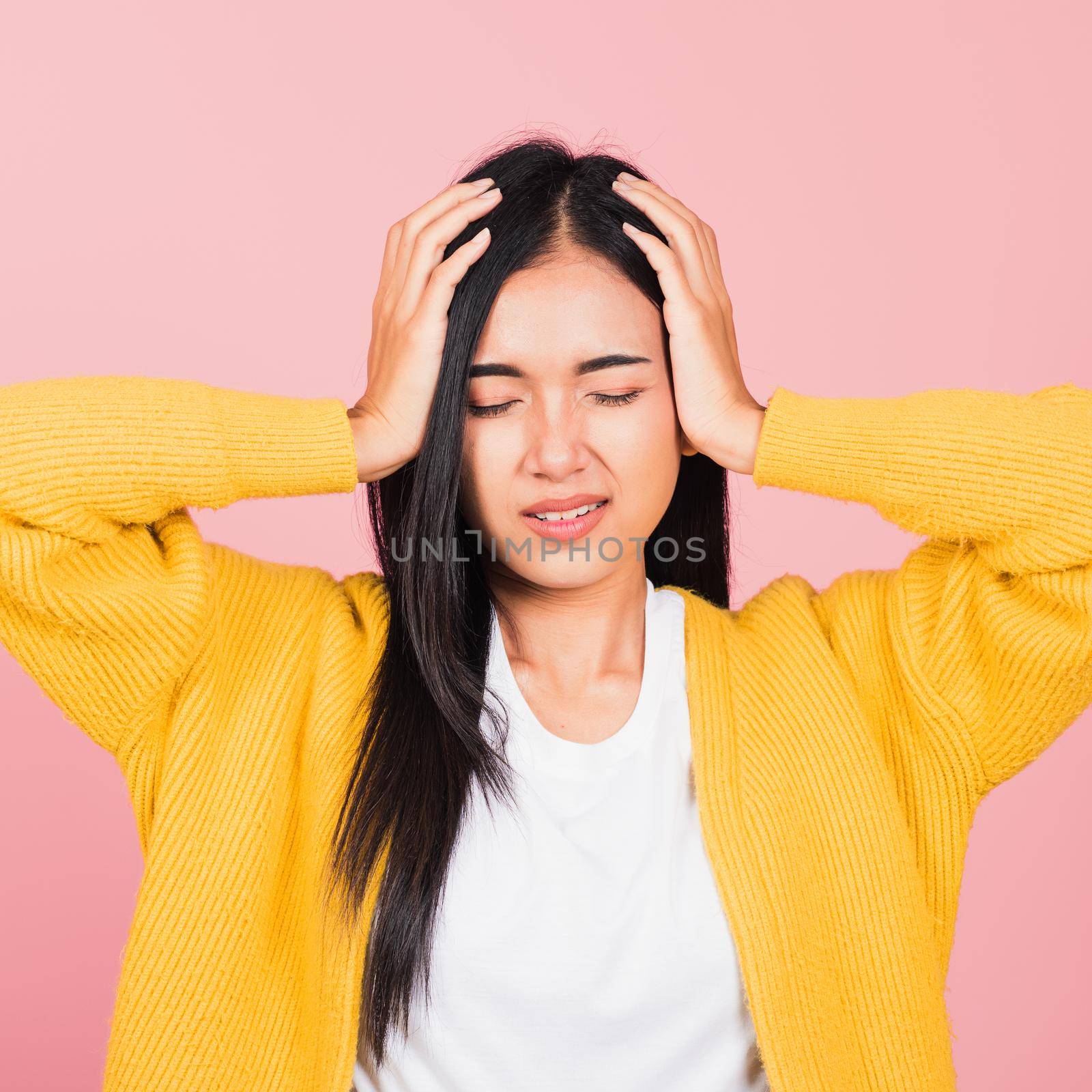 Portrait of beautiful Asian young woman sad tired strain face holding hold head by hands, female person closed eyes problem she headache, studio shot isolated on pink background