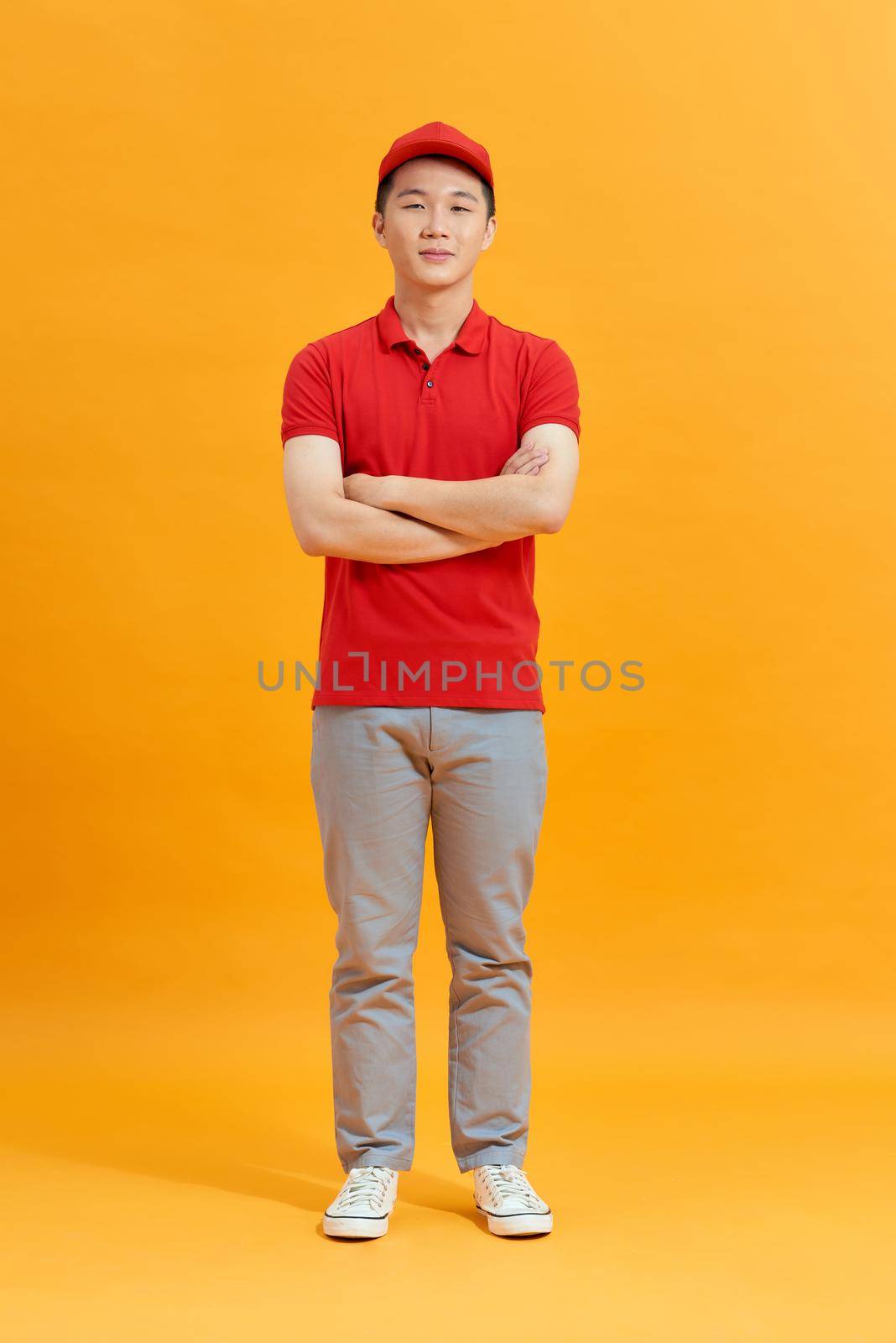 Deliveryman with arms crossed in studio. looking at camera. Full length portrait. isolated gray background by makidotvn