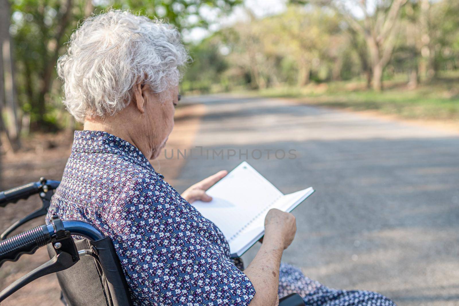 Asian senior or elderly old lady woman patient reading a book while sitting on bed in park by pamai