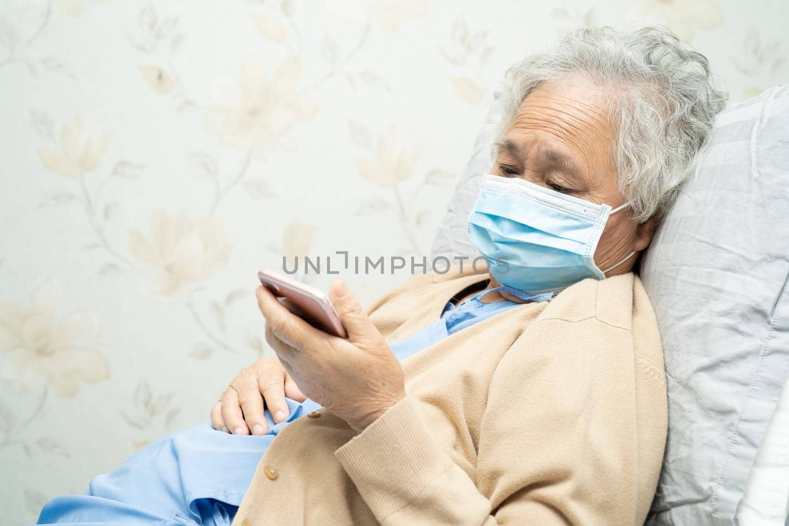 Asian senior woman patient wearing a face mask and holding mobile phone in hospital for protect safety infection and kill Novel Coronavirus Covid-19 virus.