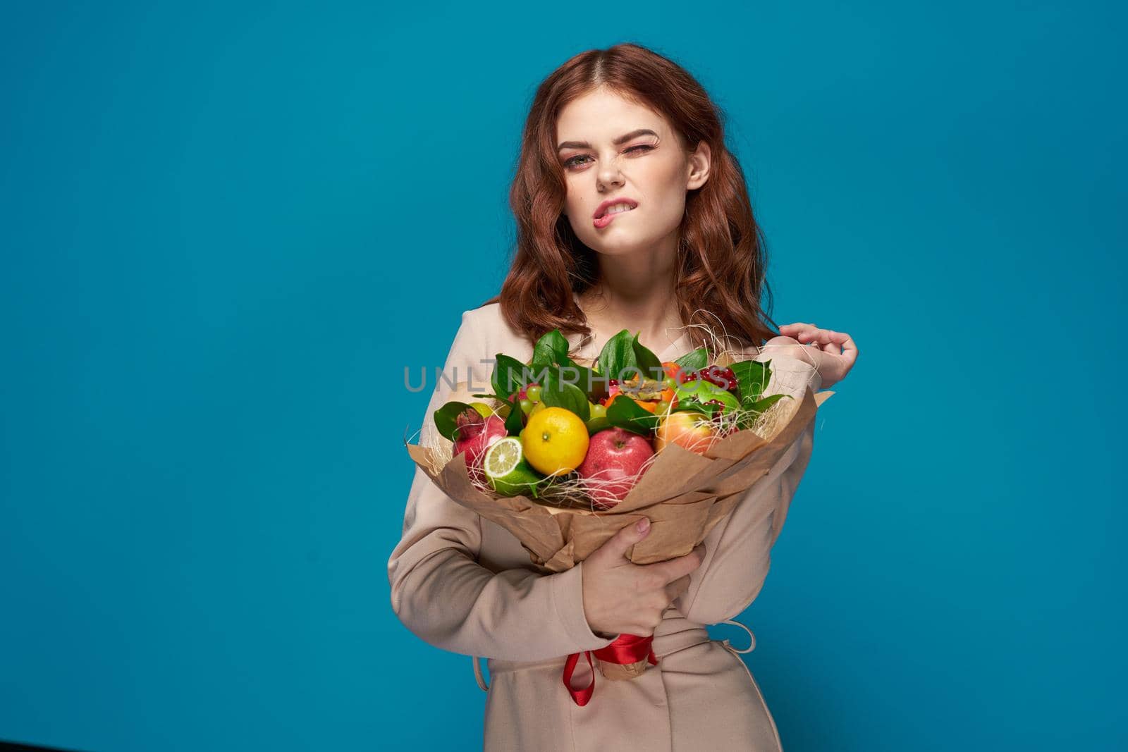 beautiful woman beige coat fruit bouquet in hands blue background. High quality photo