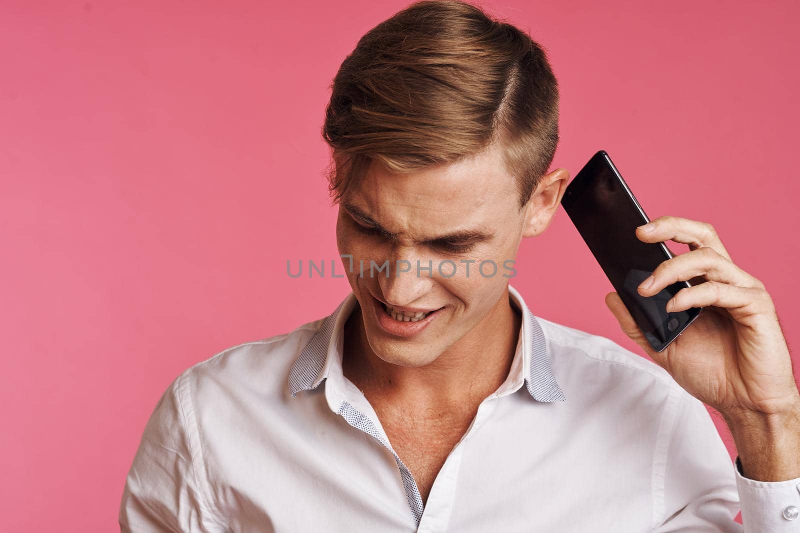 portrait of a man in a white shirt talking on the phone pink background. High quality photo