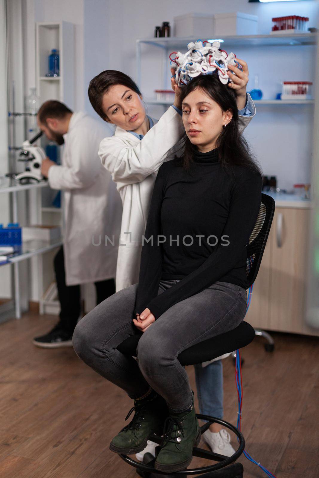 Woman patient standing on chair in neurology laboratory during clinical experiment while specialist researcher putting medical eeg scanner on head monitoring brain activity. Nervous system evolution