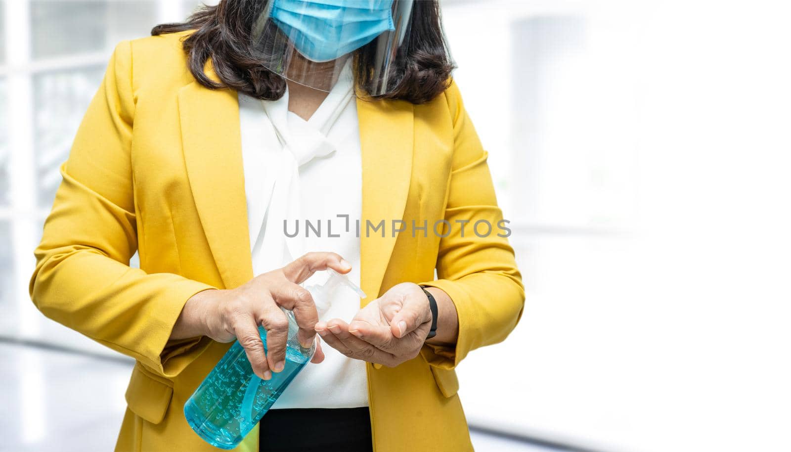 New Normal, Asian working woman with face mask washing hand by press blue alcohol sanitizer gel for protect safety infection and kill Covid-19 Coronavirus in office.