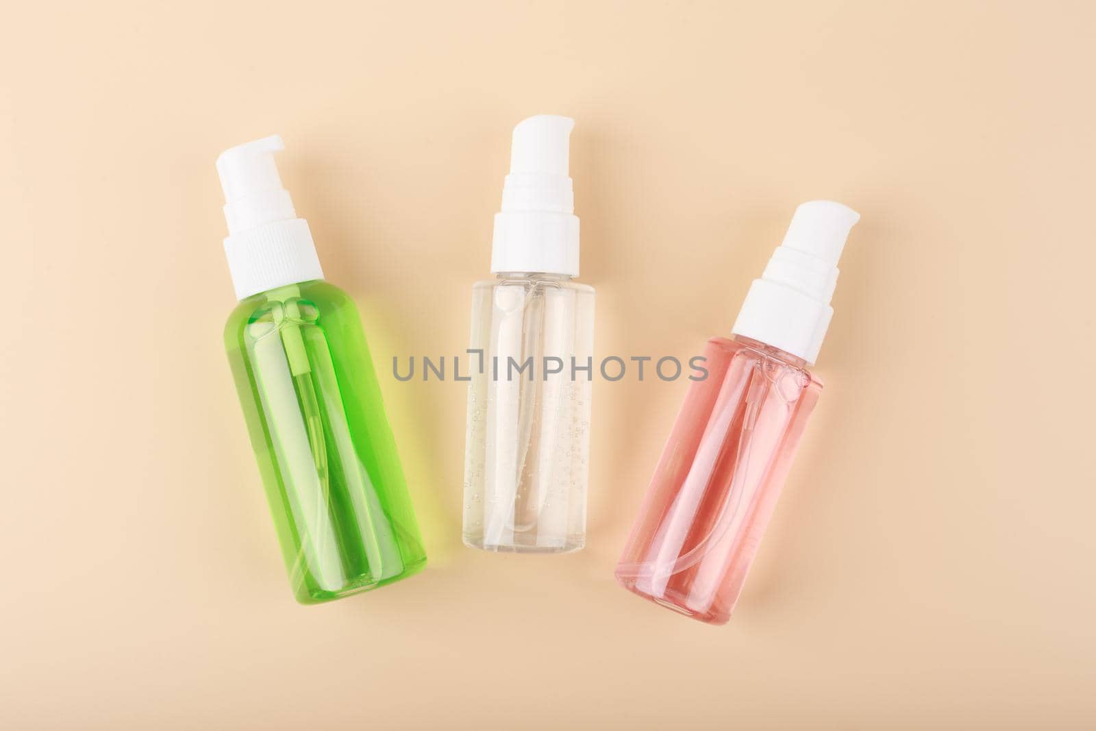 Three different face lotion, liquid foam or gel for skin cleaning in transparent tubes on bright pastel beige background. Concept of daily skin care treatment, cleaning, exfoliating and moisturizing