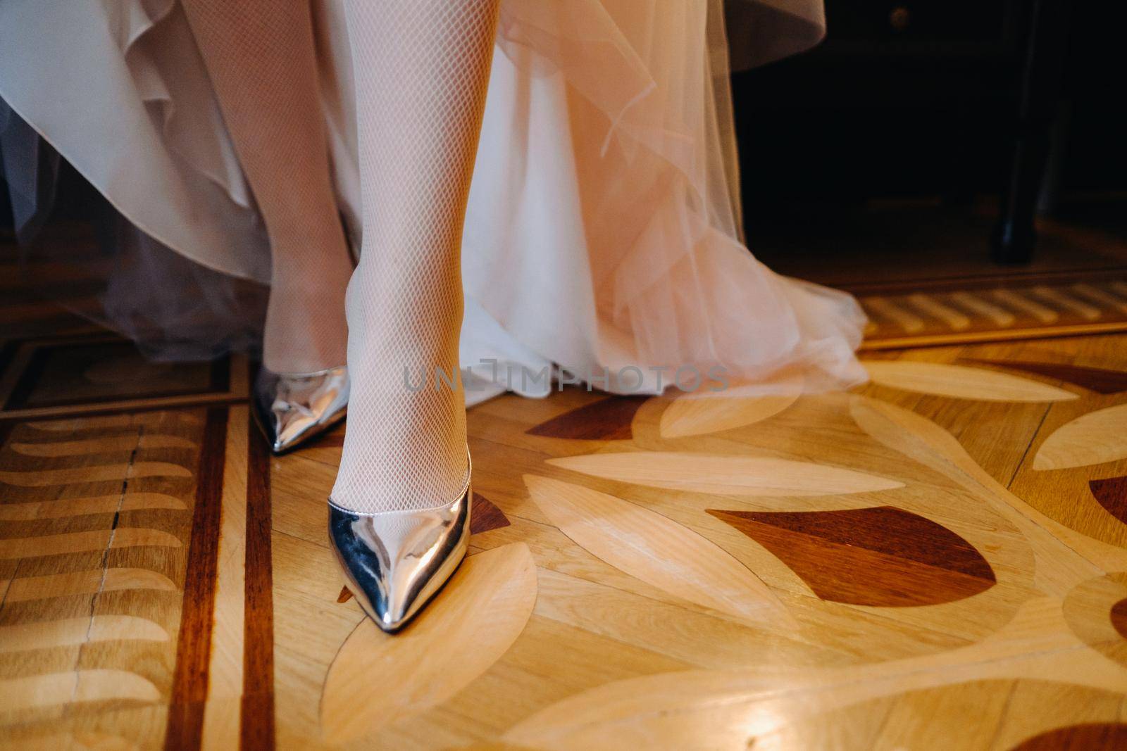 Close-up of women's shoes and the hem of a wedding dress. The bride's foot in a silver slipper by Lobachad