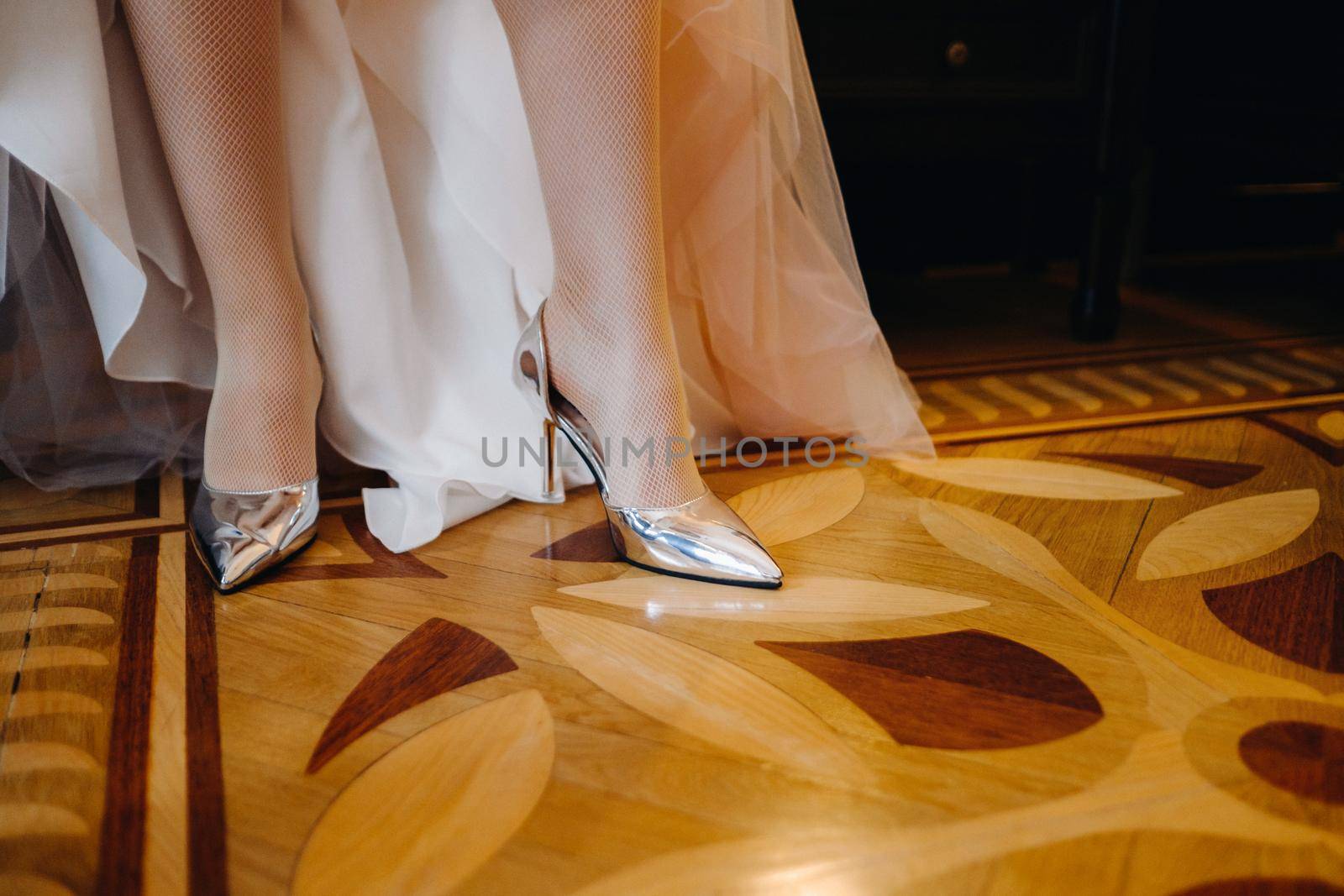 Close-up of women's shoes and the hem of a wedding dress. The bride's foot in a silver slipper by Lobachad