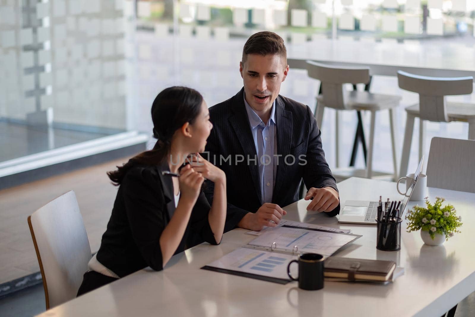 Asian and caucasian businesspeople learn new business app, apprentice listen associate tell about corporate program. Multiracial client and bank manager at business meeting using laptop negotiating.