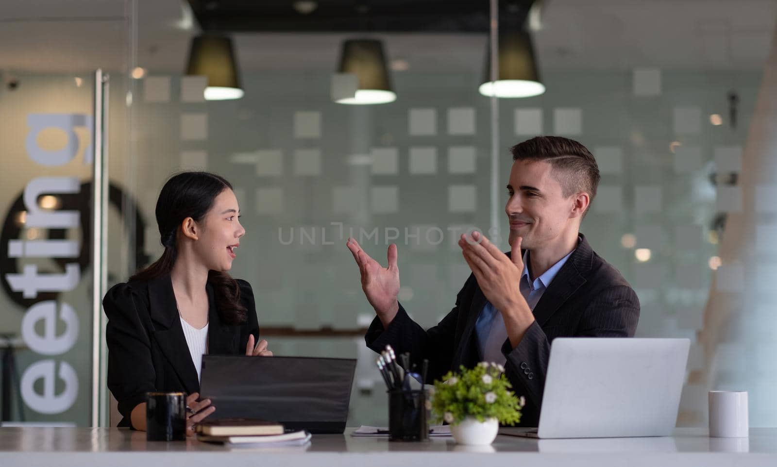 Asian and caucasian businesspeople learn new business app, apprentice listen associate tell about corporate program. Multiracial client and bank manager at business meeting using laptop negotiating.