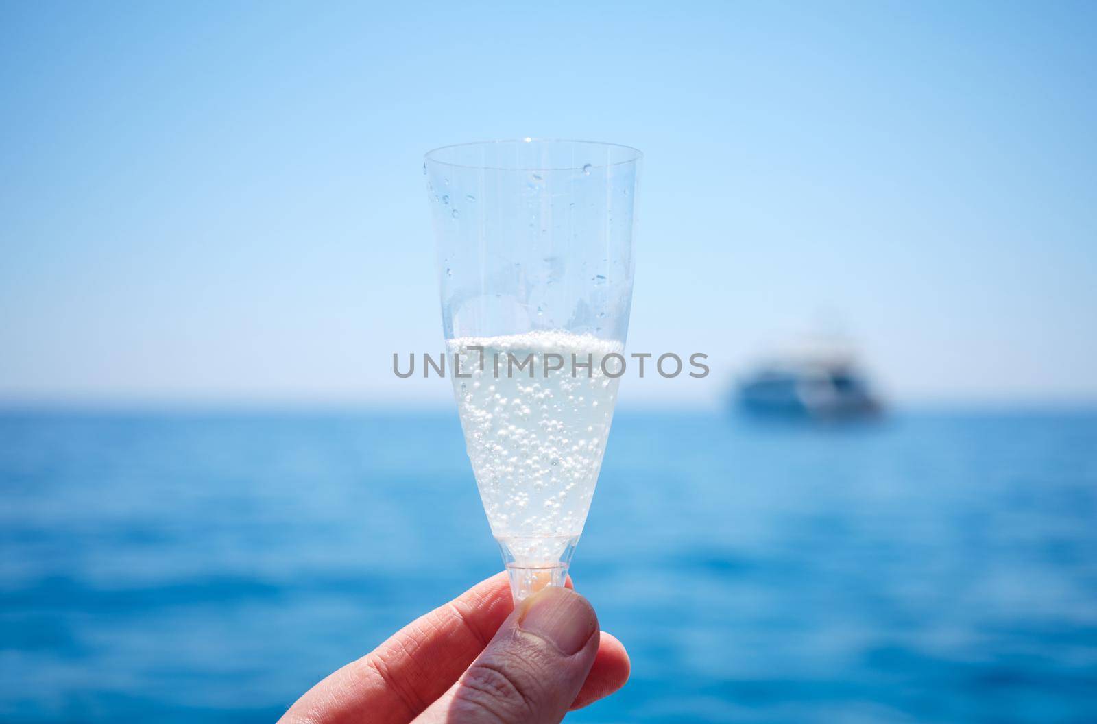 cheers in front of the sea on a sunny day - man's hand holding a glass with sparkling wine