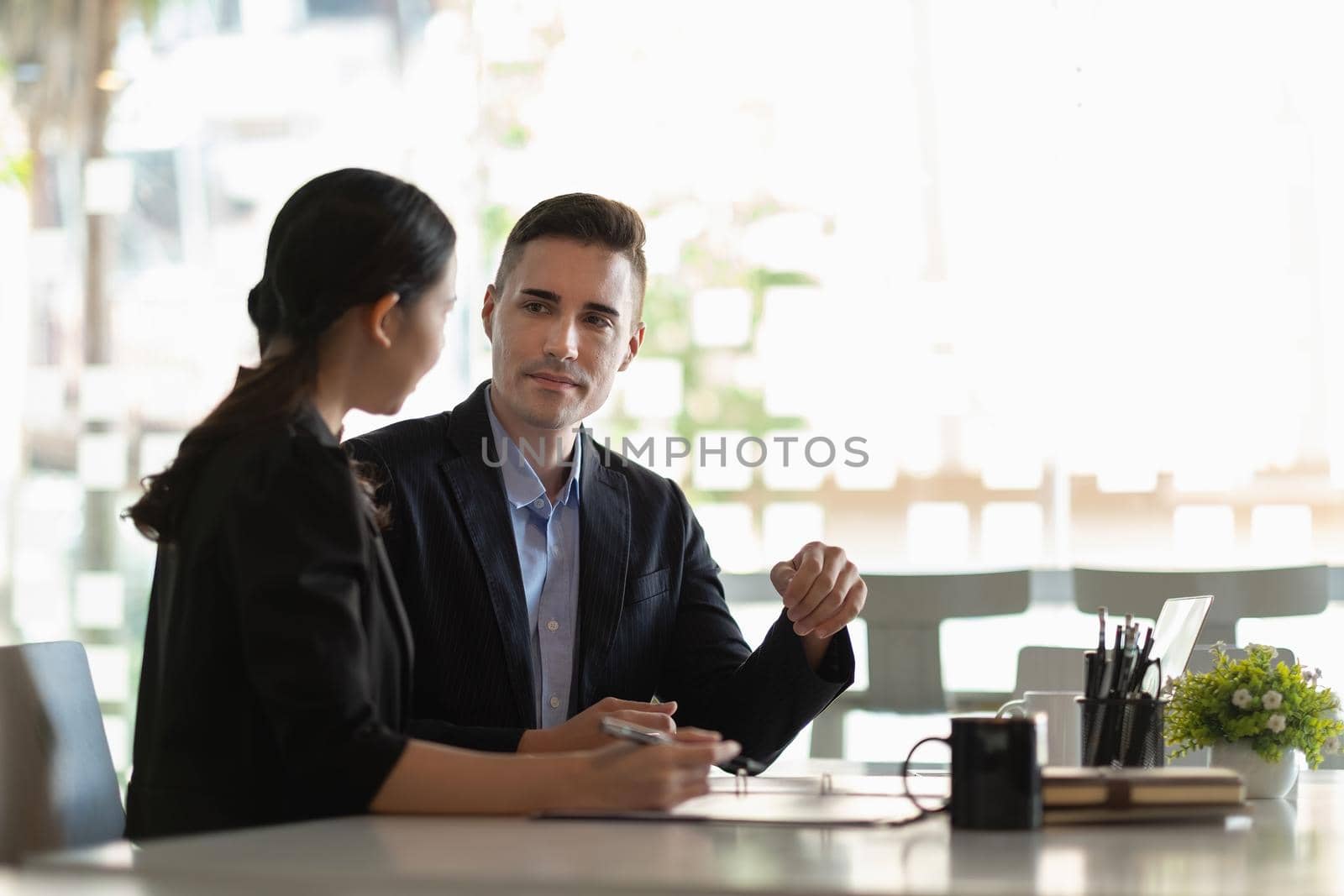 Asian and caucasian businesspeople learn new business app, apprentice listen associate tell about corporate program. Multiracial client and bank manager at business meeting using laptop negotiating.