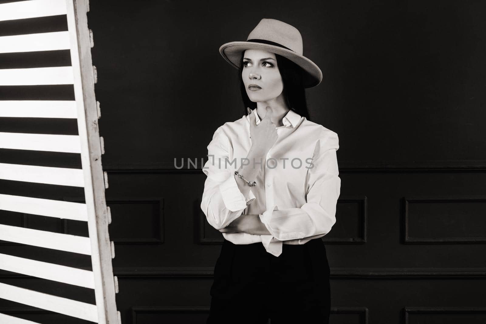 Elegant brunette girl in a white shirt and beige hat on a dark background.black and white photo.