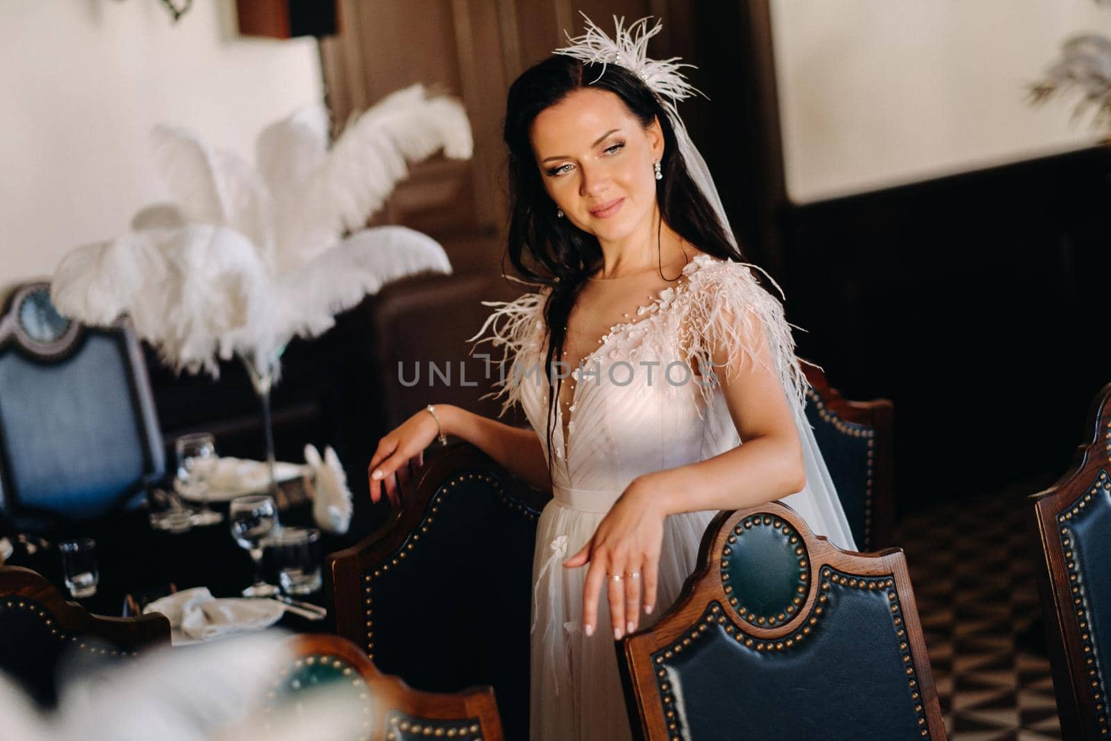 A stylish bride in a wedding dress in the interior of a restaurant decorated with feathers on the tables.