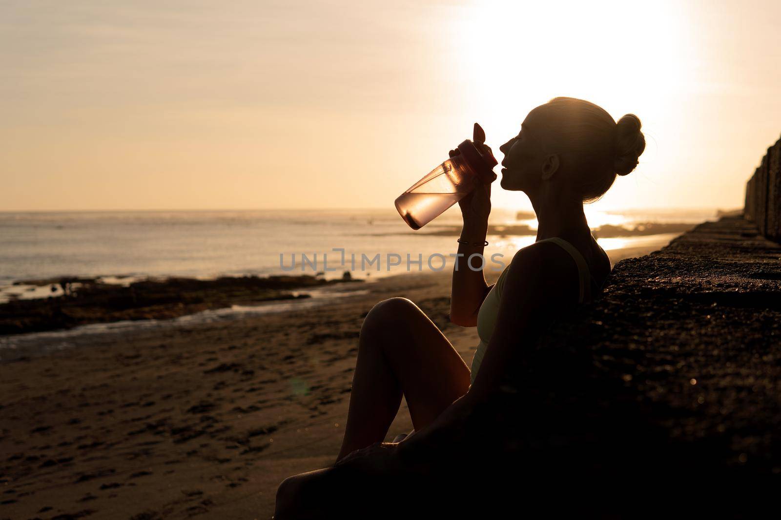 beautiful young woman drinking water. bali sunset
