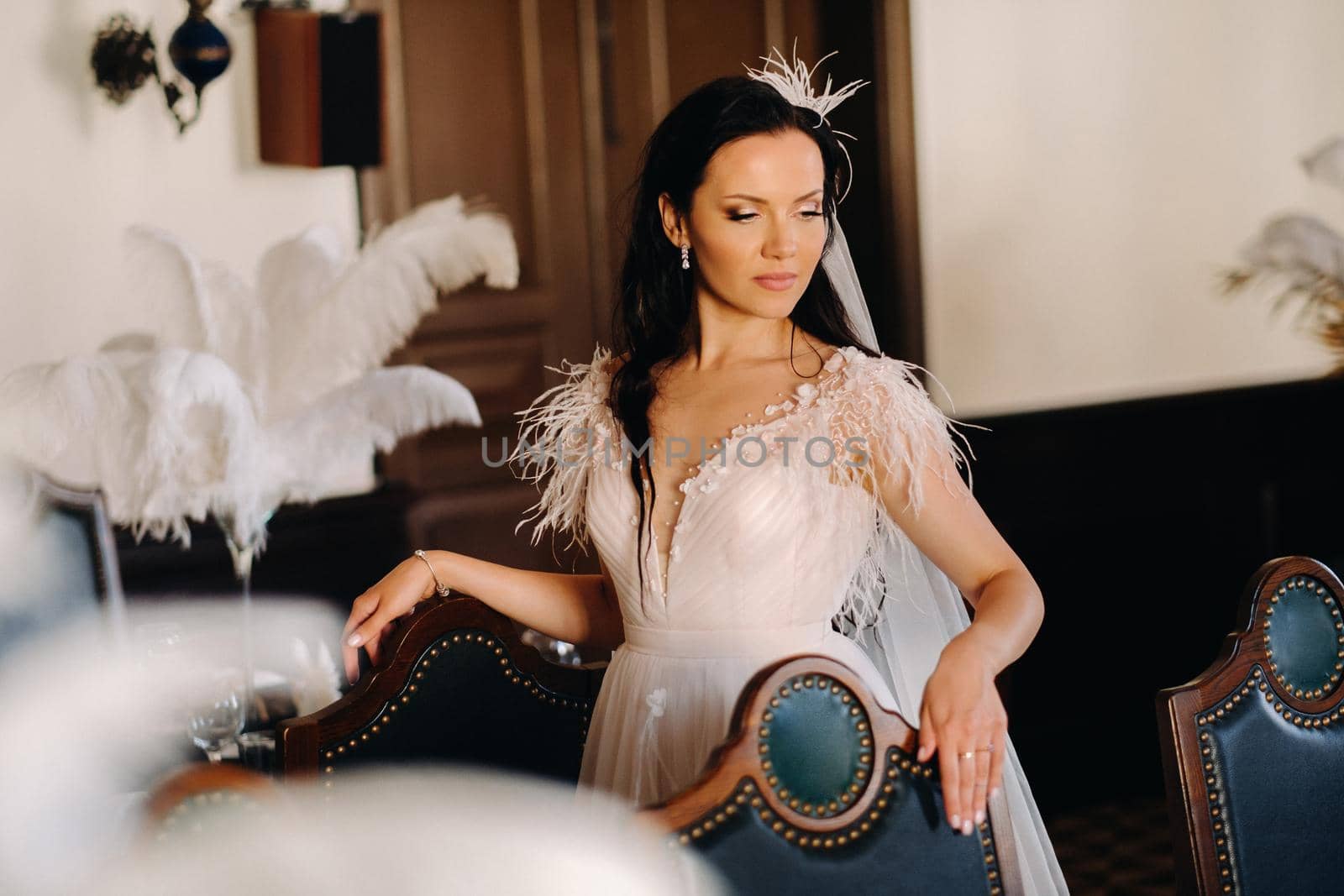 A stylish bride in a wedding dress in the interior of a restaurant decorated with feathers on the tables.