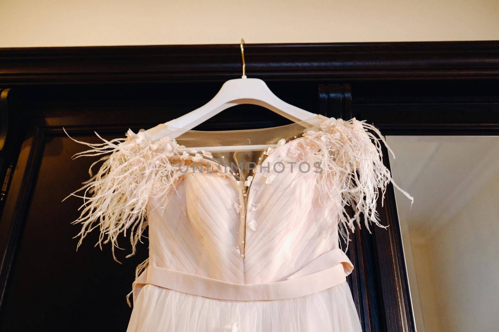Stylish wedding dress hanging on a wooden hanger in the interior.