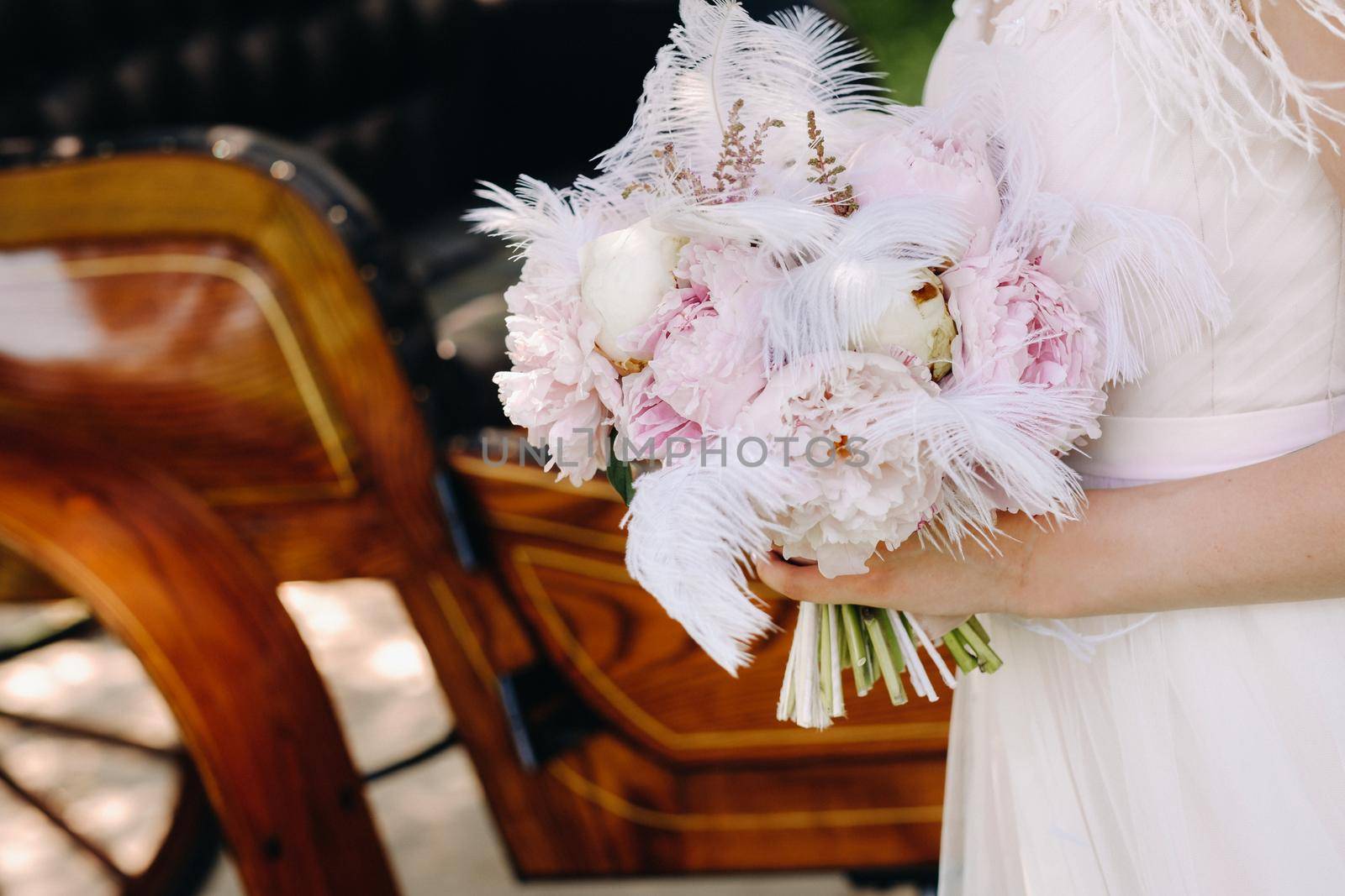 Close-up of a wedding bouquet of roses decorated with white feathers in the hands of the bride.