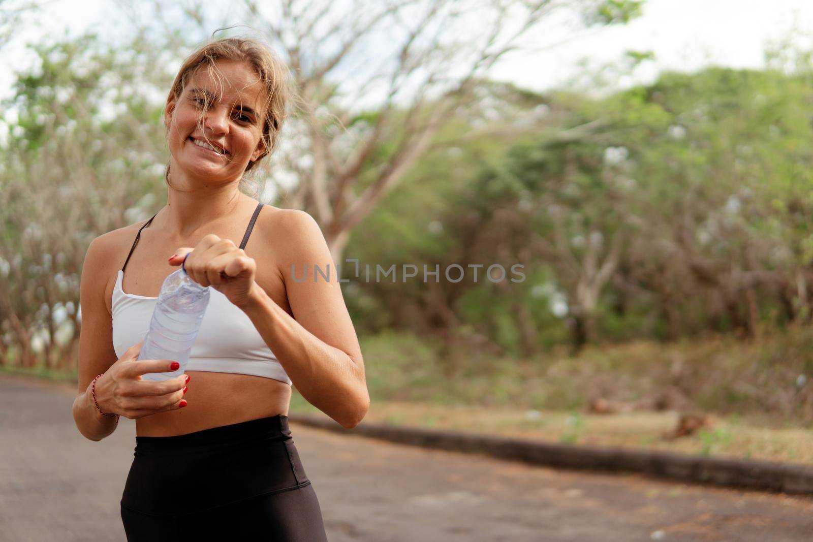 Woman drinking water in the park. by Alexzhilkin