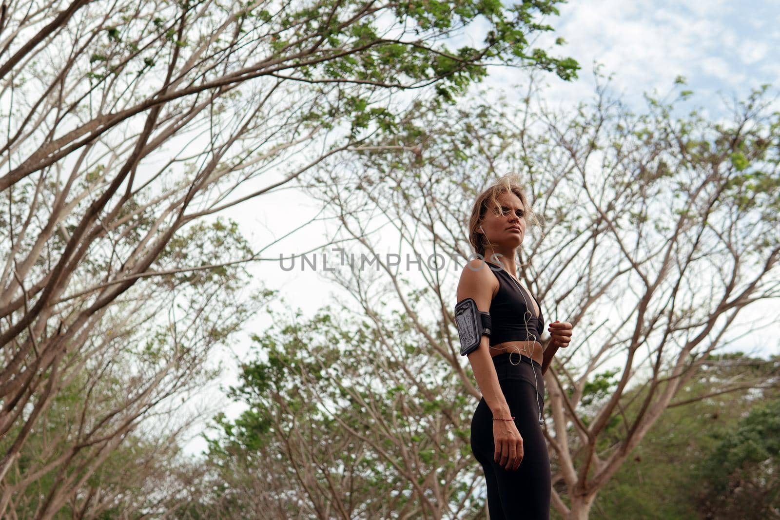 Beautiful woman in black sportwear listening to music in the forest by Alexzhilkin