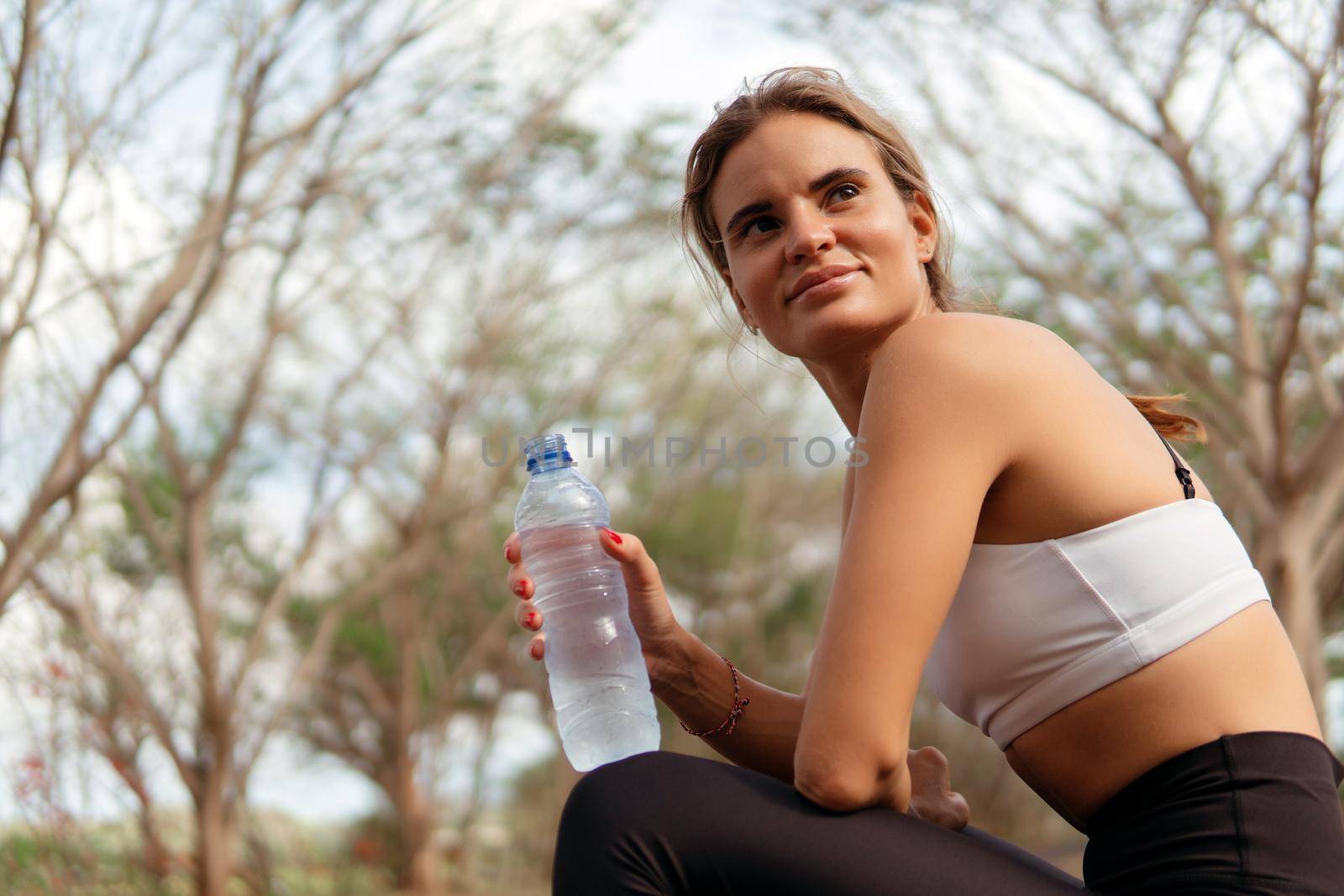 Woman drinking water in the park by Alexzhilkin