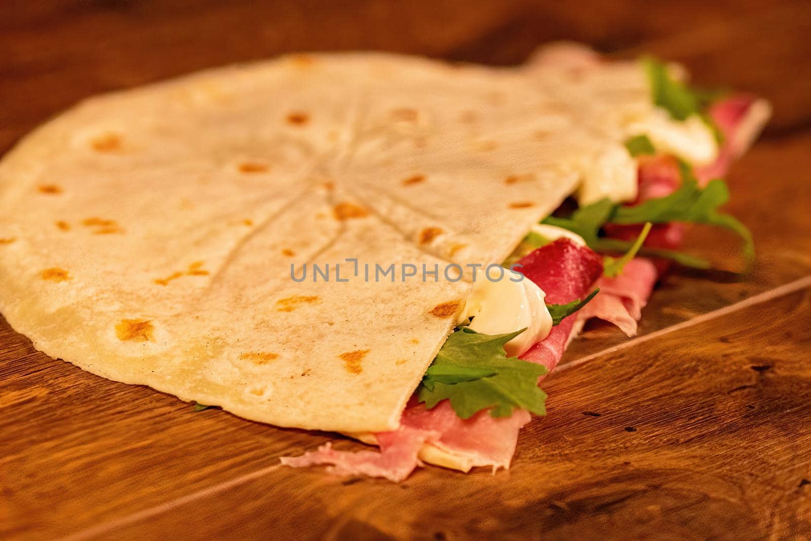 salty piadina with cured meats and vegetables on a wooden surface