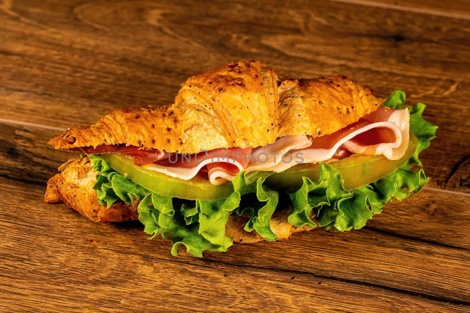 sandwich with salami and vegetables on a wooden surface