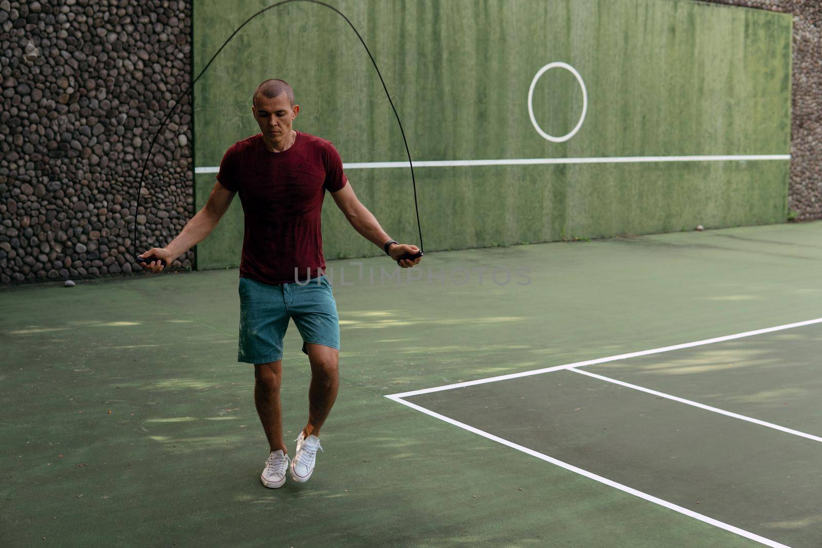 man jumping rope on the tennis court by Alexzhilkin