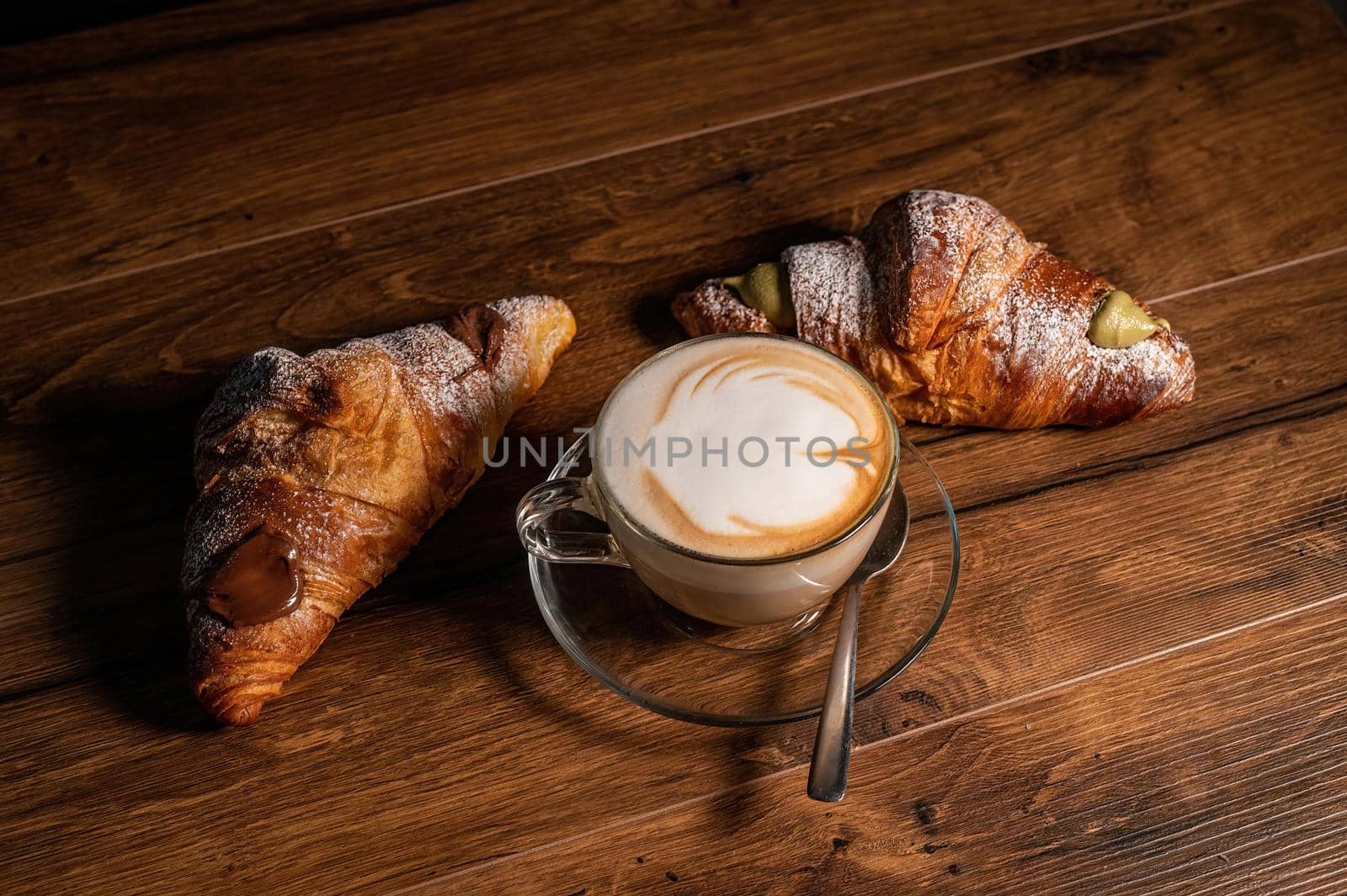 sweet croissants with cream and cappuccino on a wooden surface