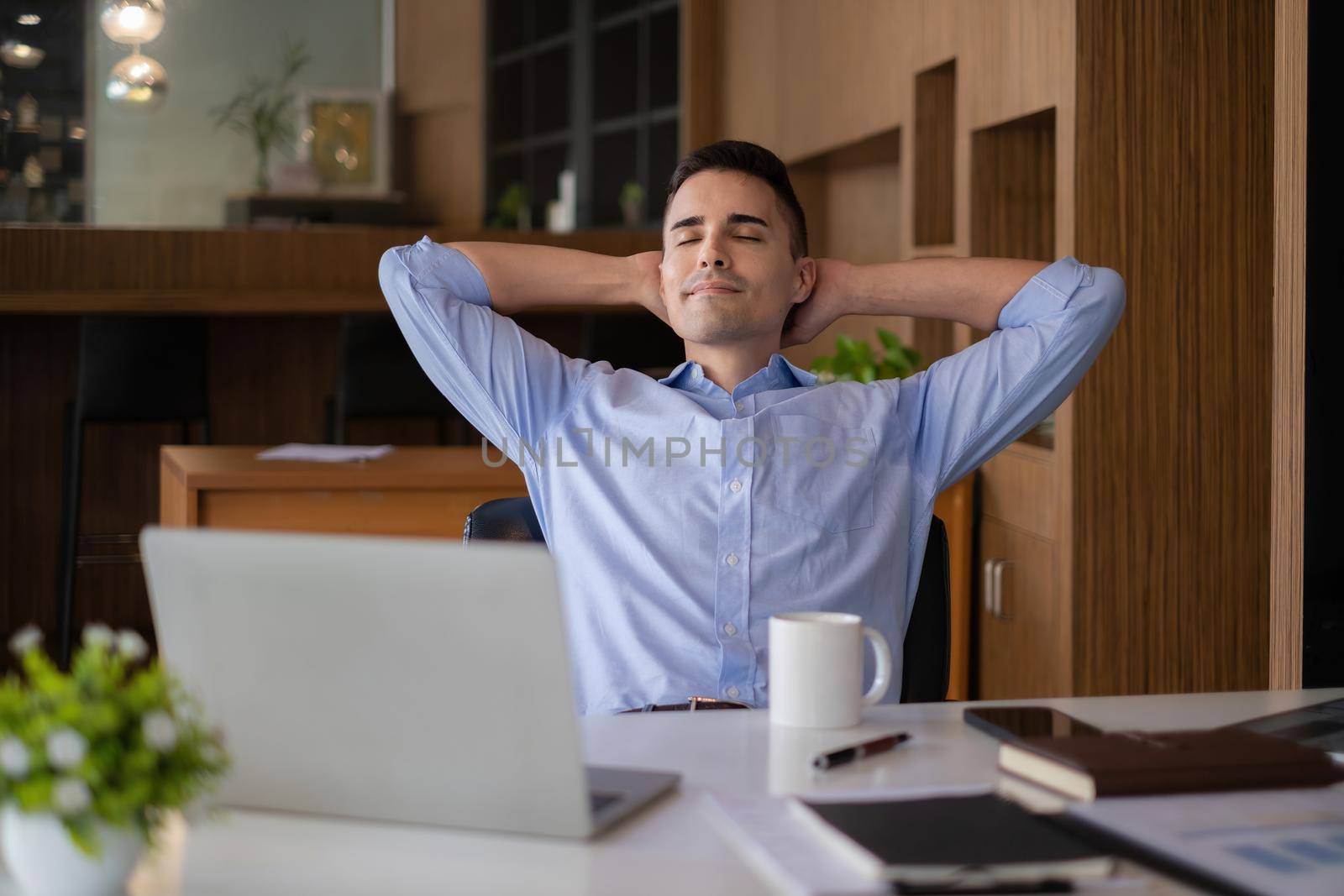 American businessman relaxing in chair after hard work at offlice. Business man with laptop on desk by itchaznong