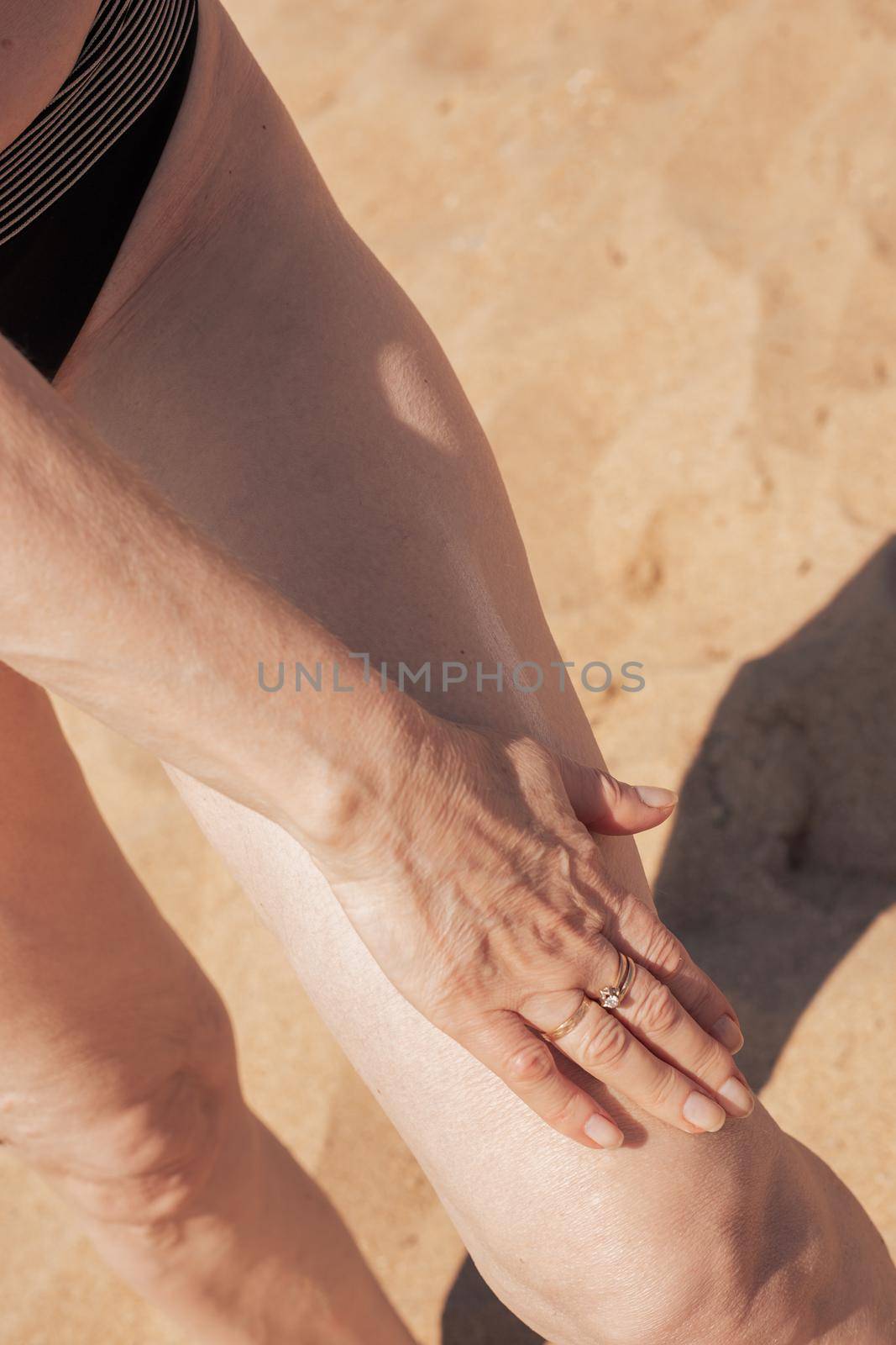 Mature woman with sagging skin smears her legs with sunscreen. Protecting the skin from the bright sun.
