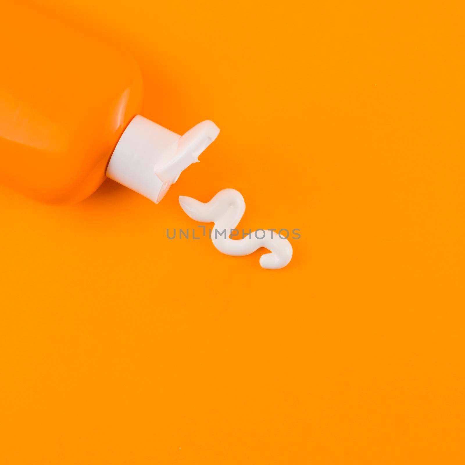 white sunscreen cream coming out orange bottle against orange backdrop. High quality photo by Zahard