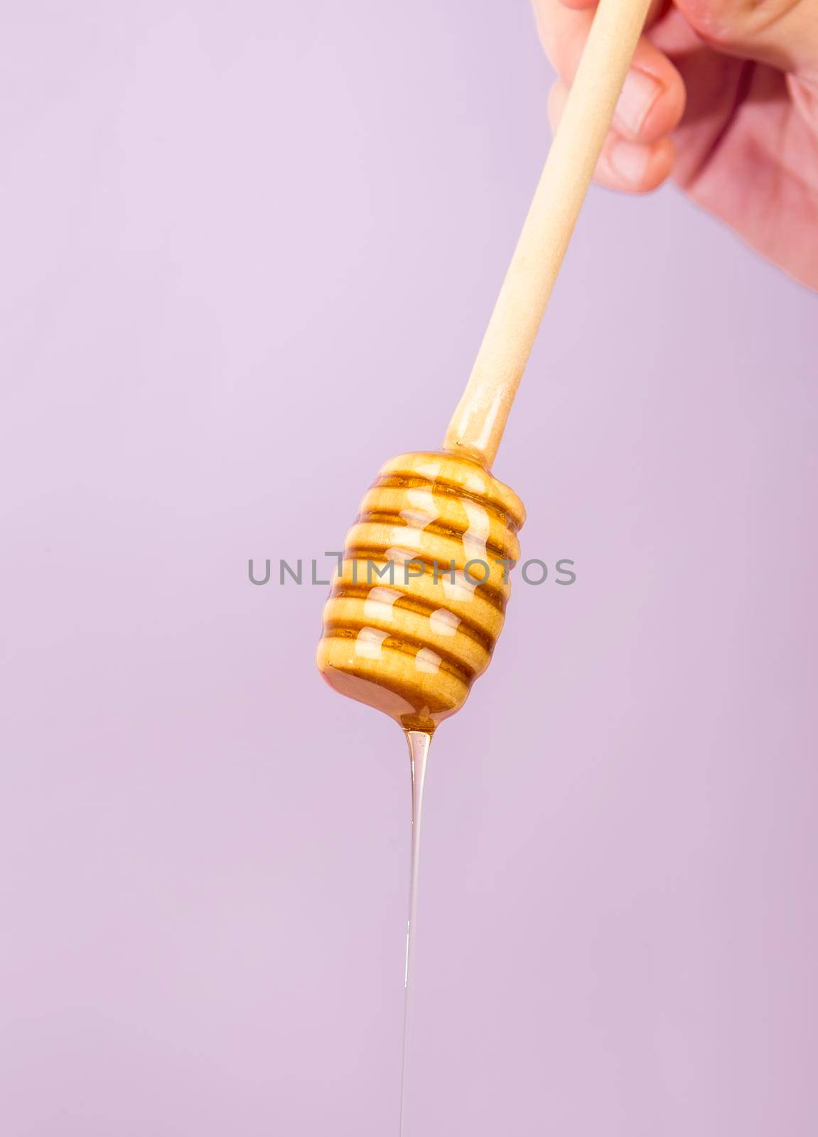 human hand holding dipper with honey purple backdrop. High resolution photo