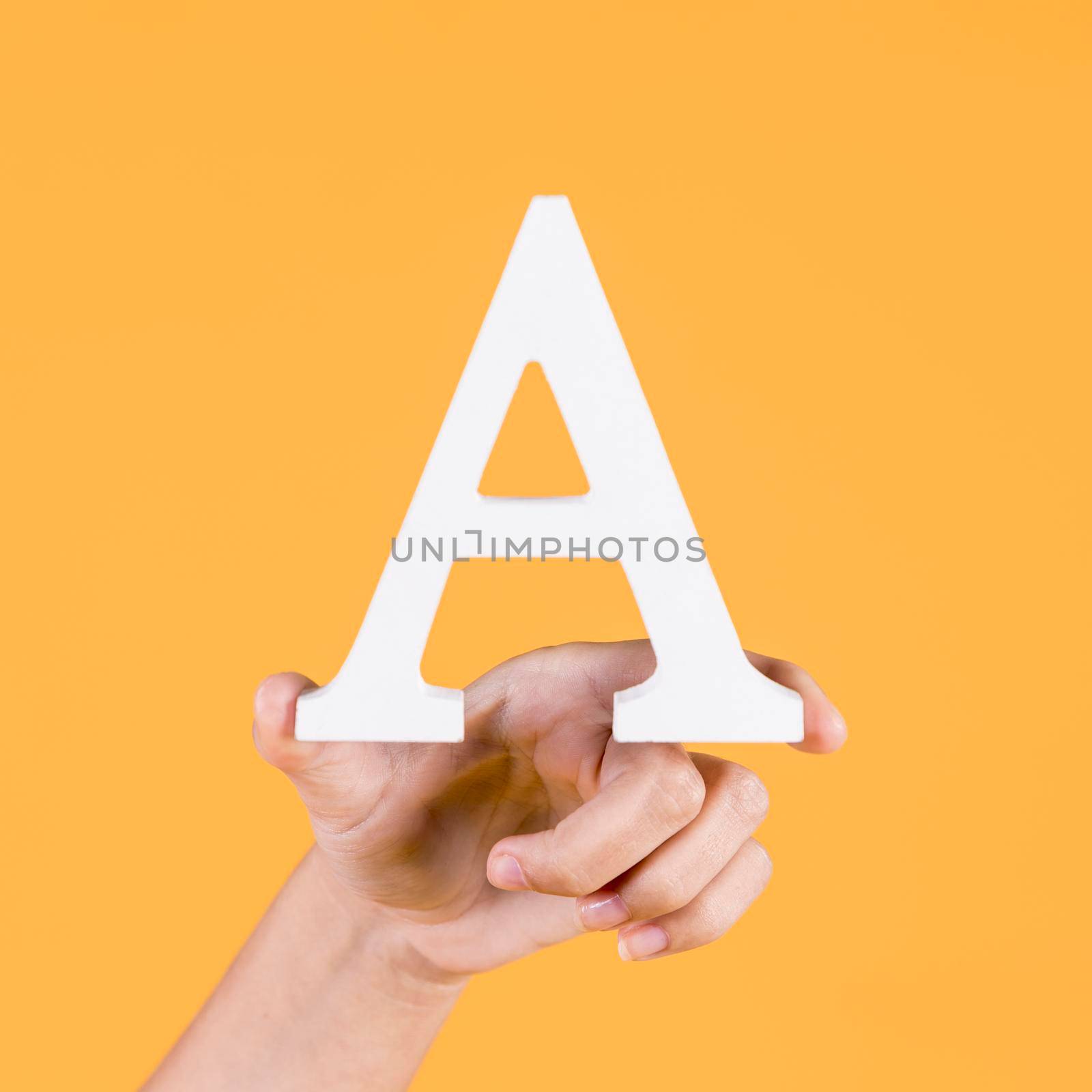 human hand holding up uppercase capital letter yellow background. High resolution photo