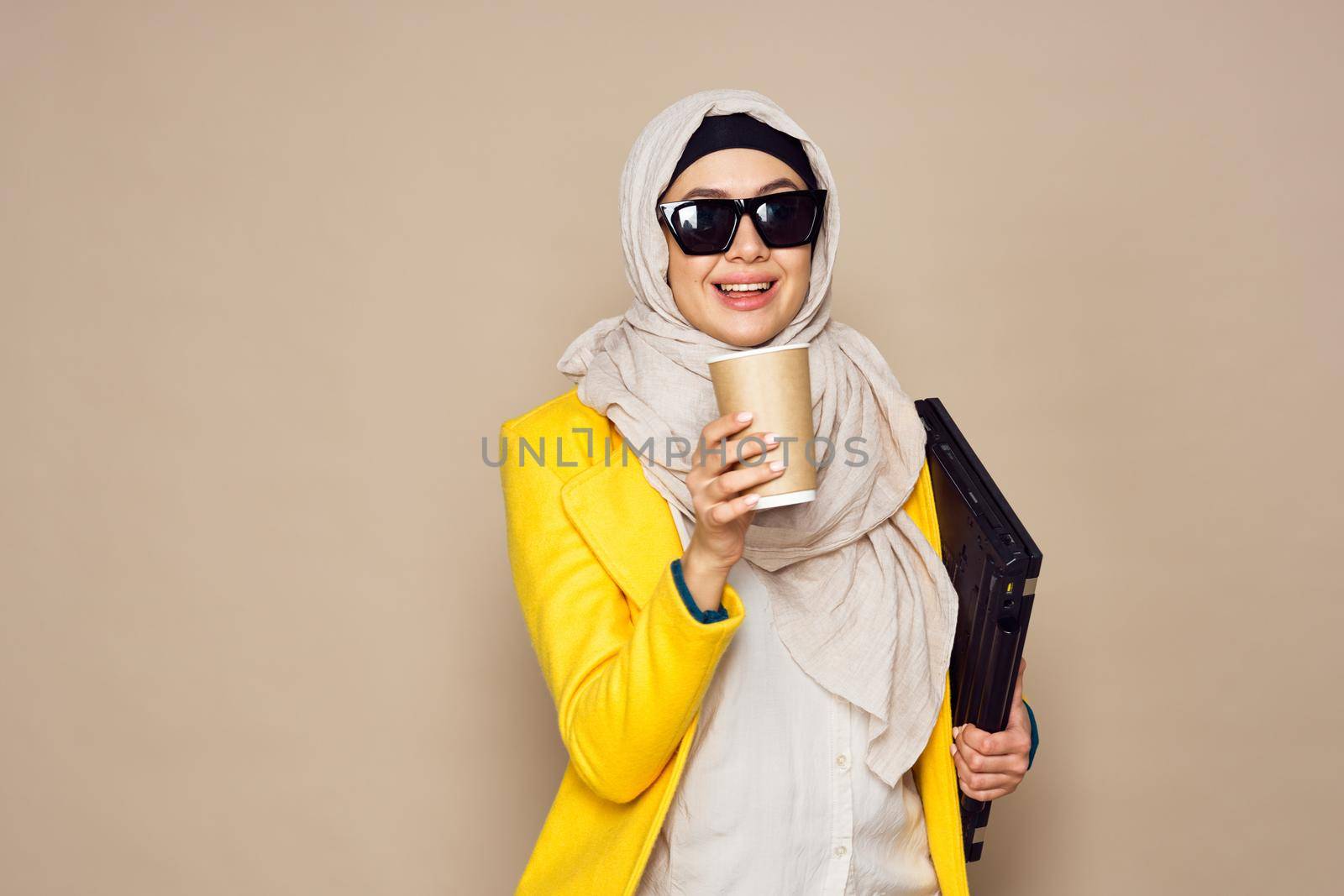 woman in sunglasses in hijab a cup of coffee beige background. High quality photo