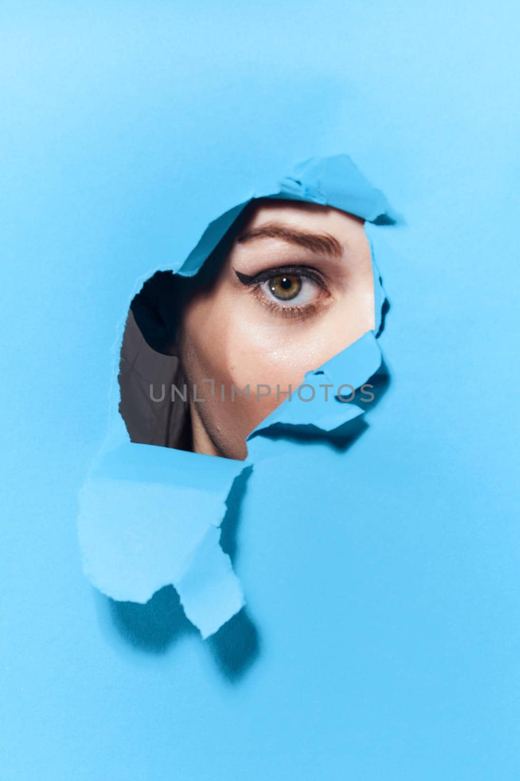 woman peeping through the holes in the poster blue studio background. High quality photo