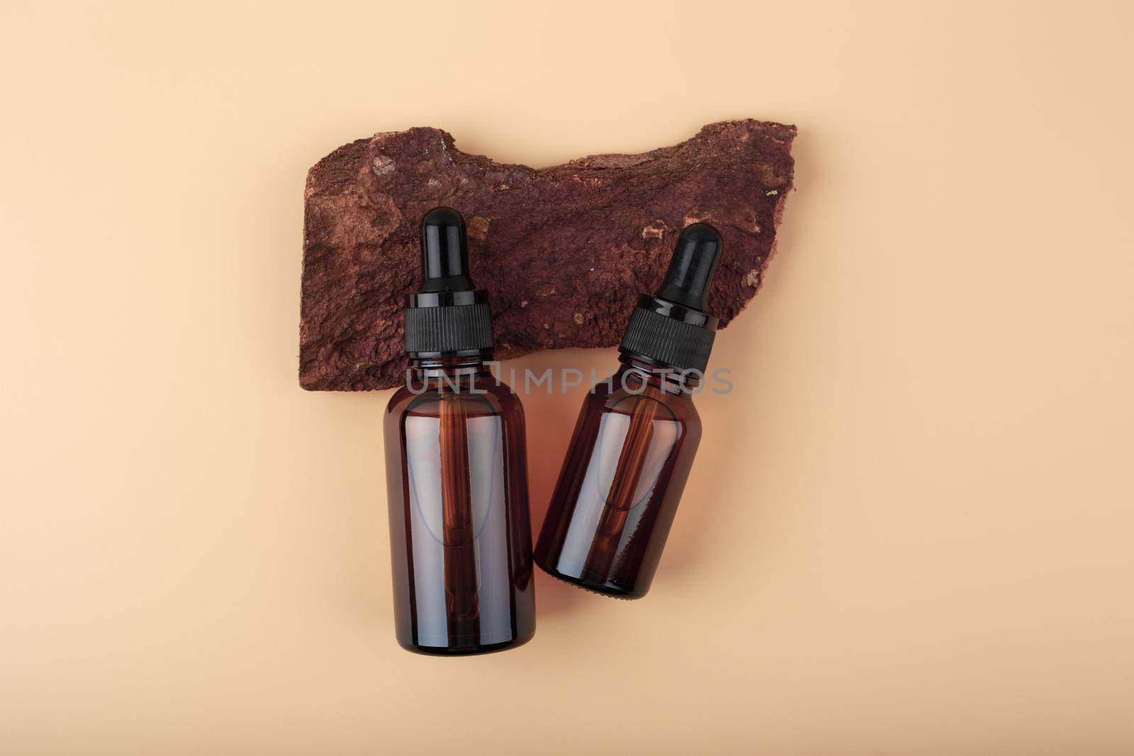 Two transparent dark brown glass bottles with skin serum or oil for manicure on dark piece of wood on beige background by Senorina_Irina