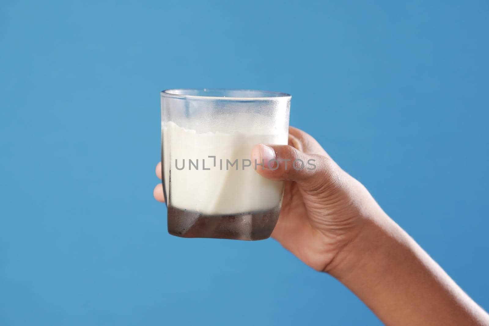 child boy hand hold a glass of milk against blue background .