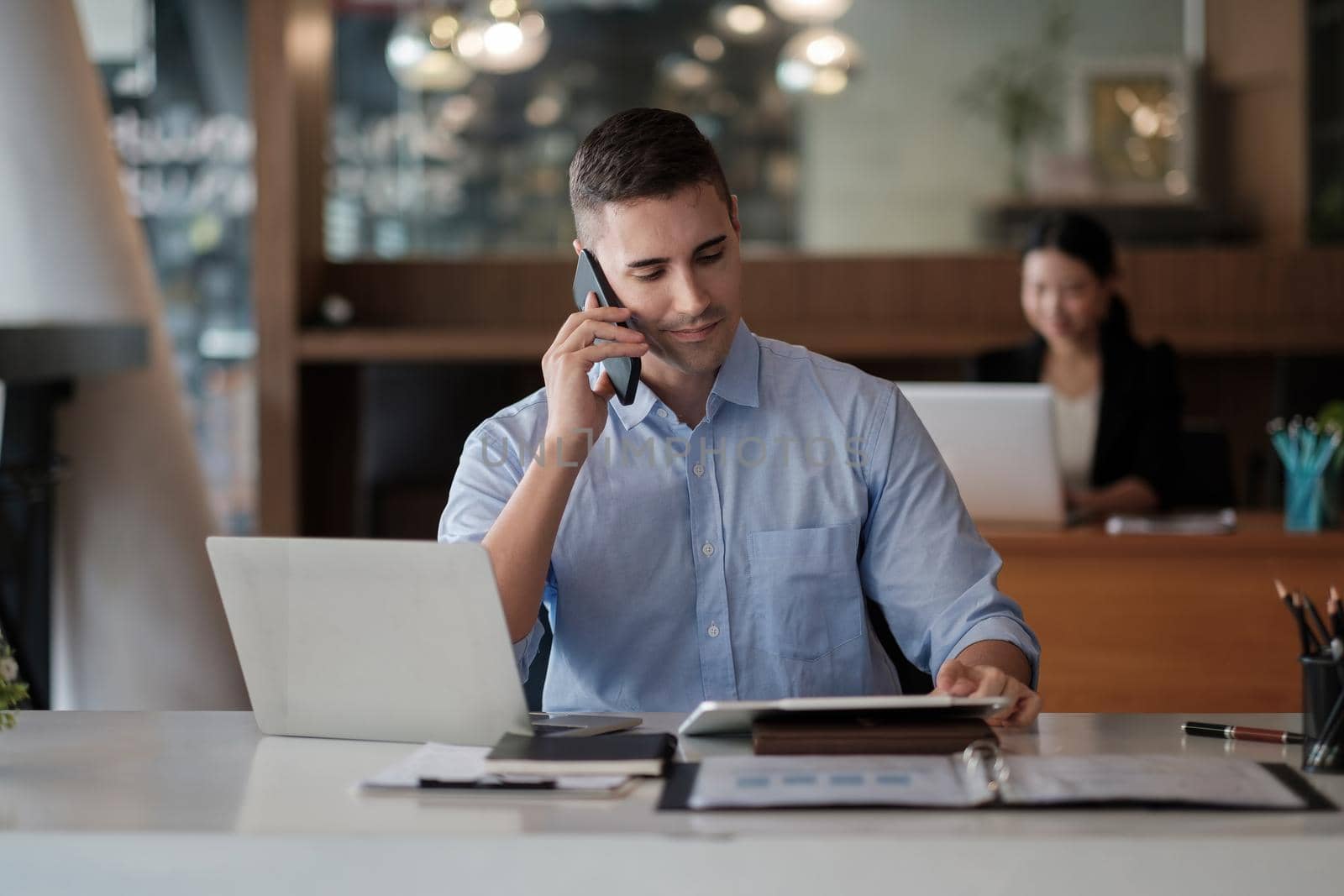 Portrait of young smiling cheerful entrepreneur in modern office making phone call while working with laptop