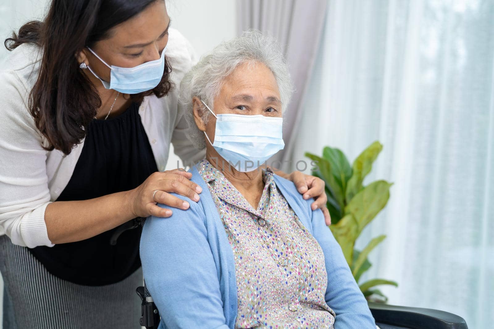 Caregiver help Asian senior or elderly old lady woman sitting on wheelchair and wearing a face mask for protect safety infection Covid-19 Coronavirus.