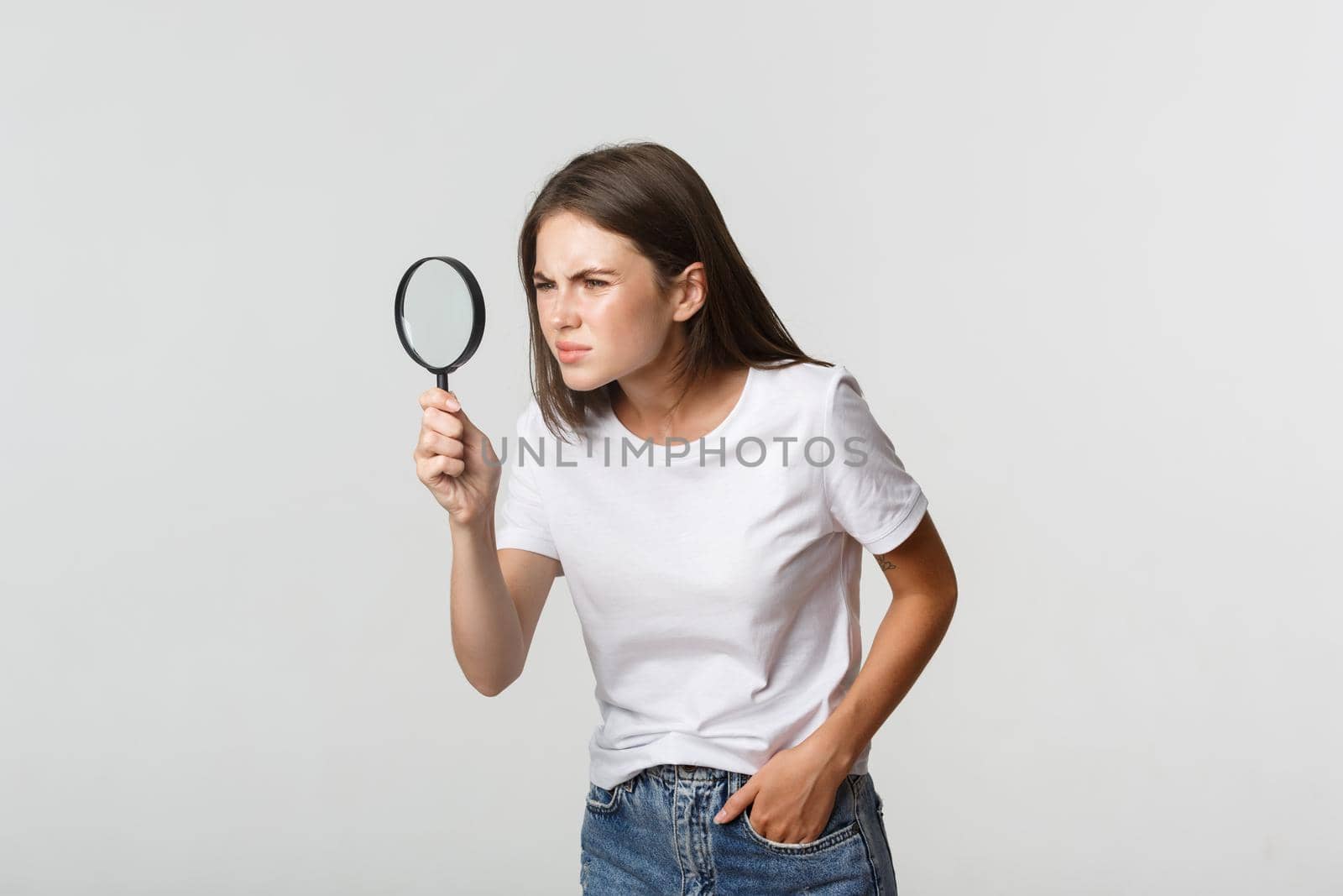 Serious-looking attractive young woman searching for something, looking through magnifying glass, white background by Benzoix