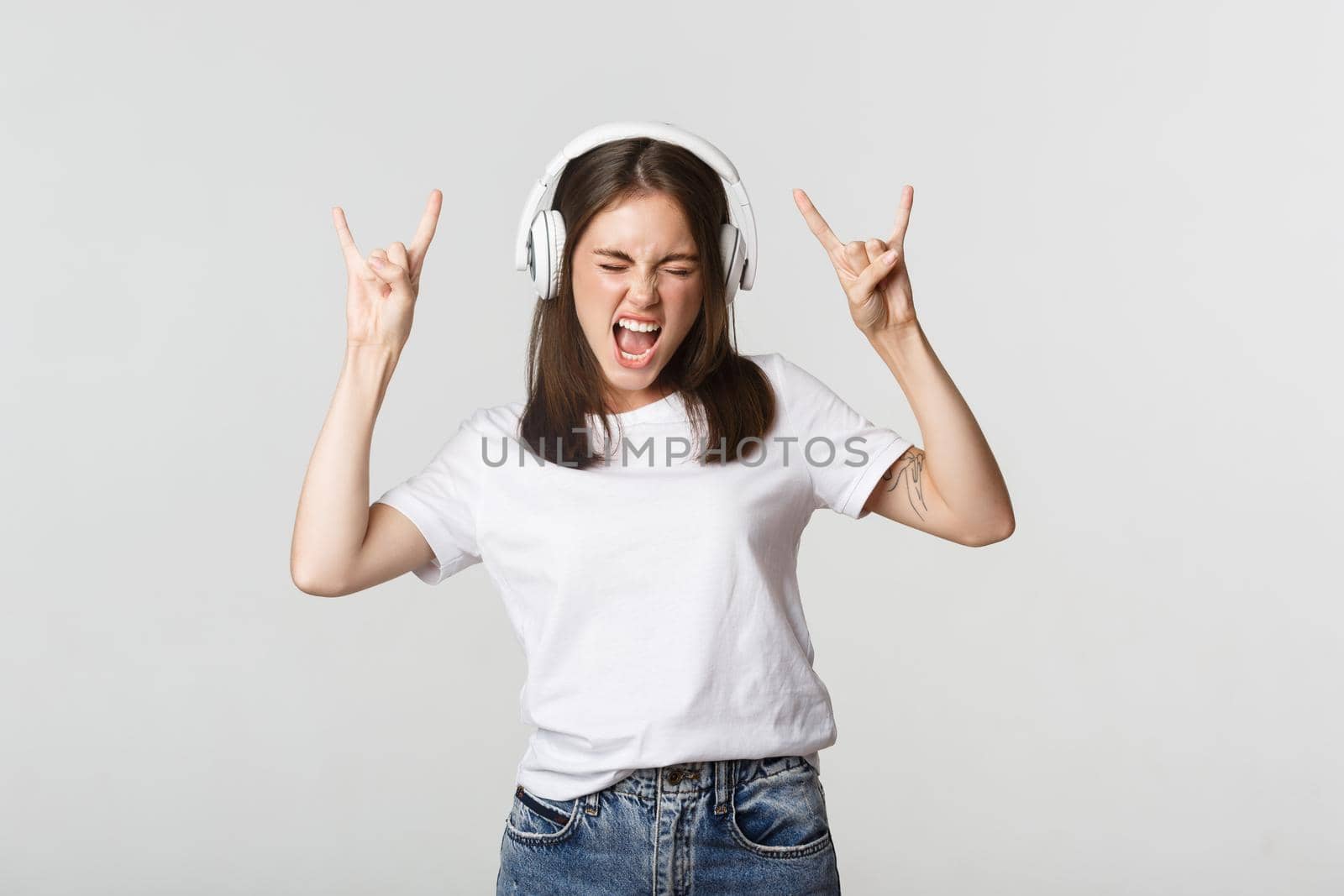 Joyful beautiful girl in headphones dancing, showing rock-n-roll signs by Benzoix