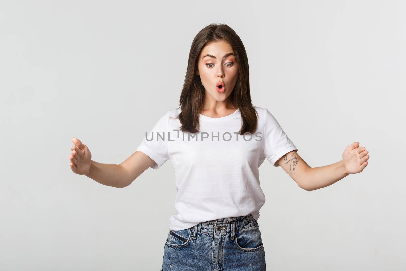 Impressed brunette girl showing large object, holding something big.