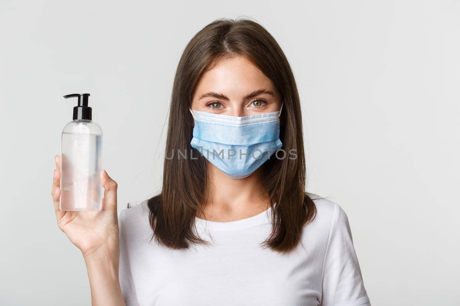Covid-19, health and social distancing concept. Close-up of attractive smiling girl in medical mask, showing hand sanitizer, recommend antiseptic.