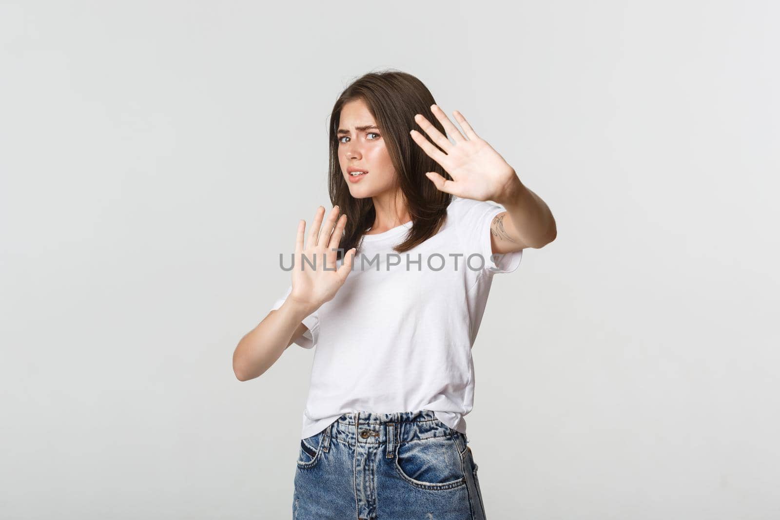 Scared and insecure cute girl raising hands in stop gesture, defending herself.