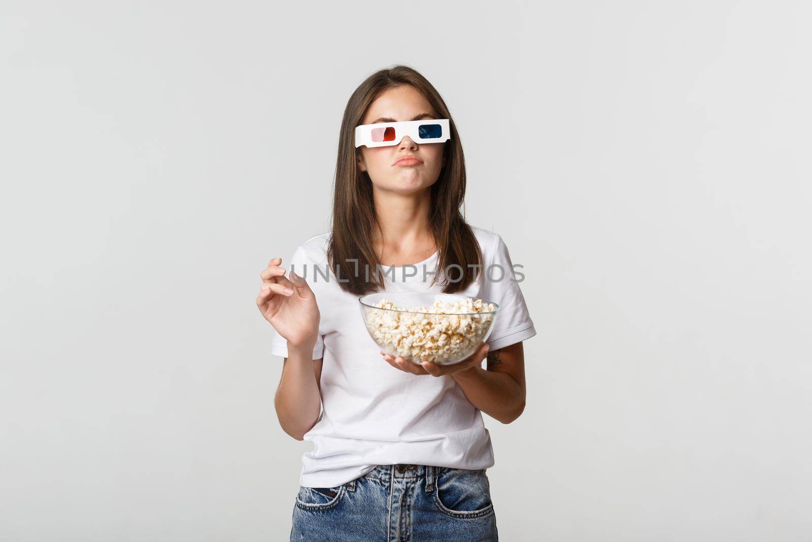 Skeptical beautiful woman in 3d glasses, holding popcorn and looking perplexed, thinking while watching movie by Benzoix