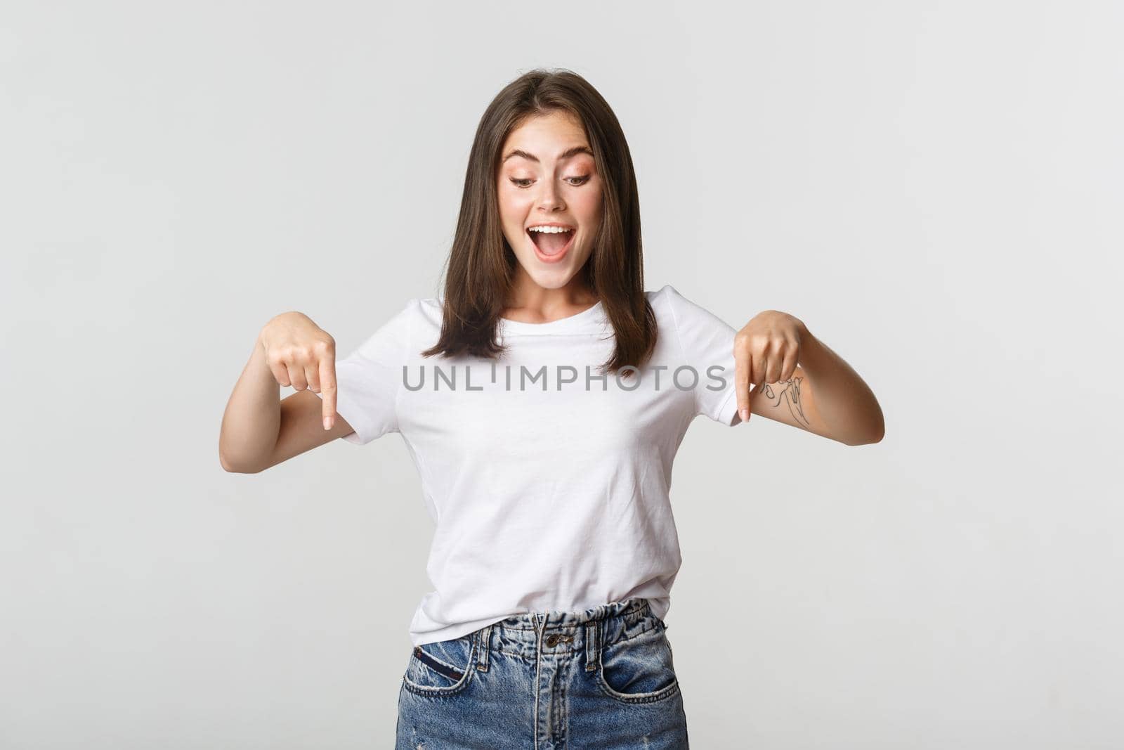 Excited happy brunette girl, looking and pointing down with amused smile.