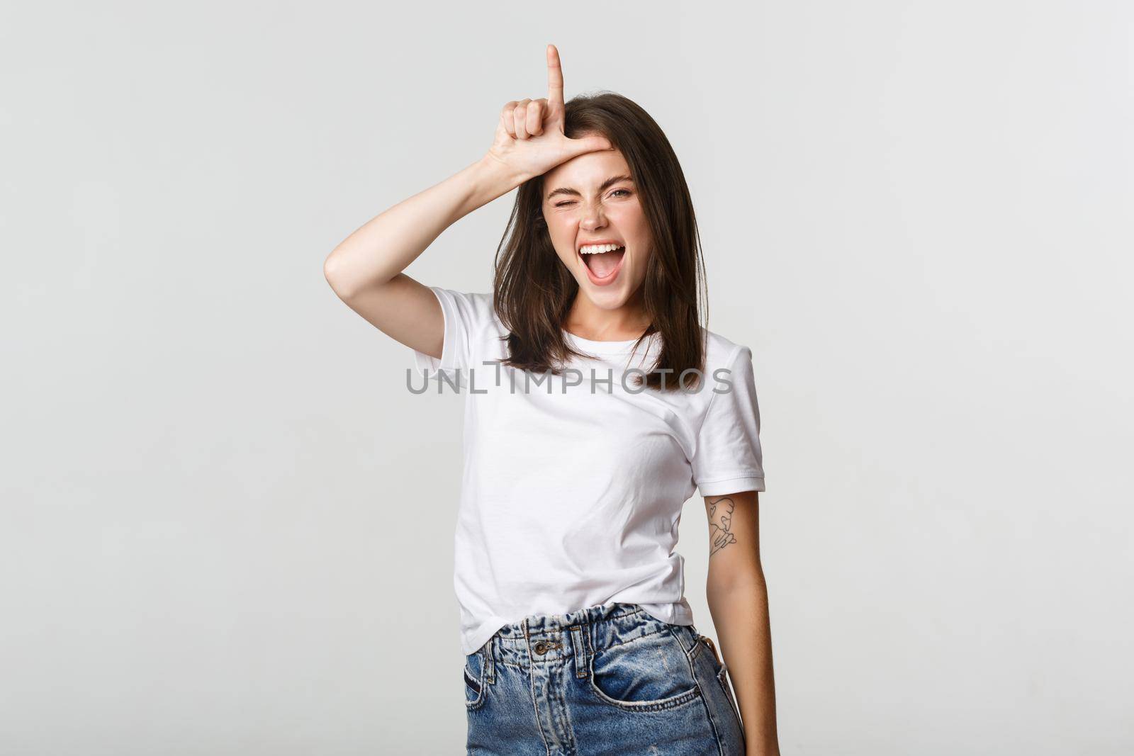 Sassy good-looking girl smiling and mocking person, showing loser gesture on forehead by Benzoix