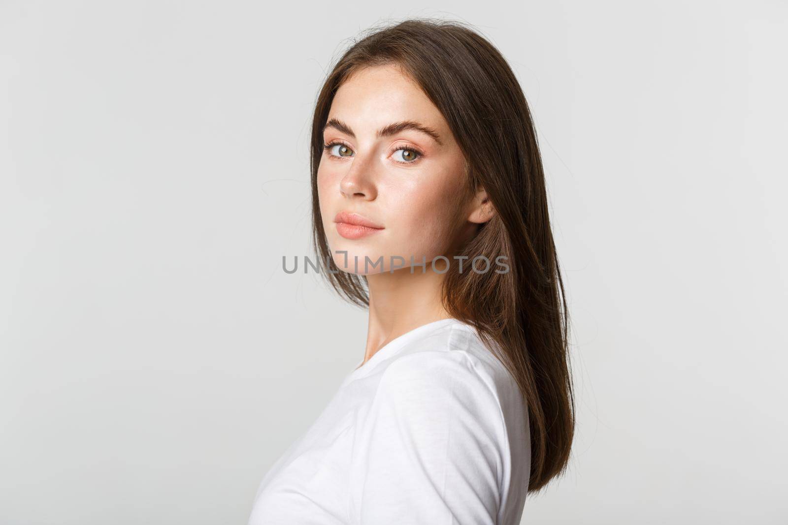 Portrait of confident beautiful brunette woman turning face at camera with dreamy look, white background by Benzoix