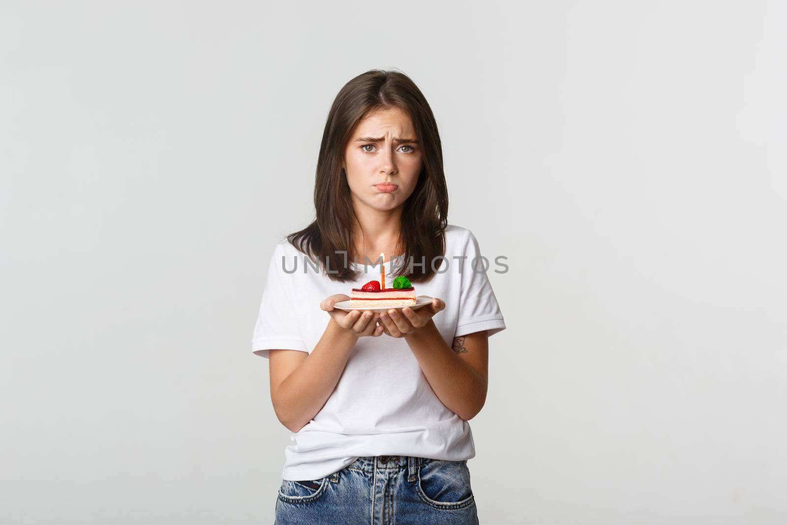 Miserable birthday girl looking sad, holding b-day cake with candle.