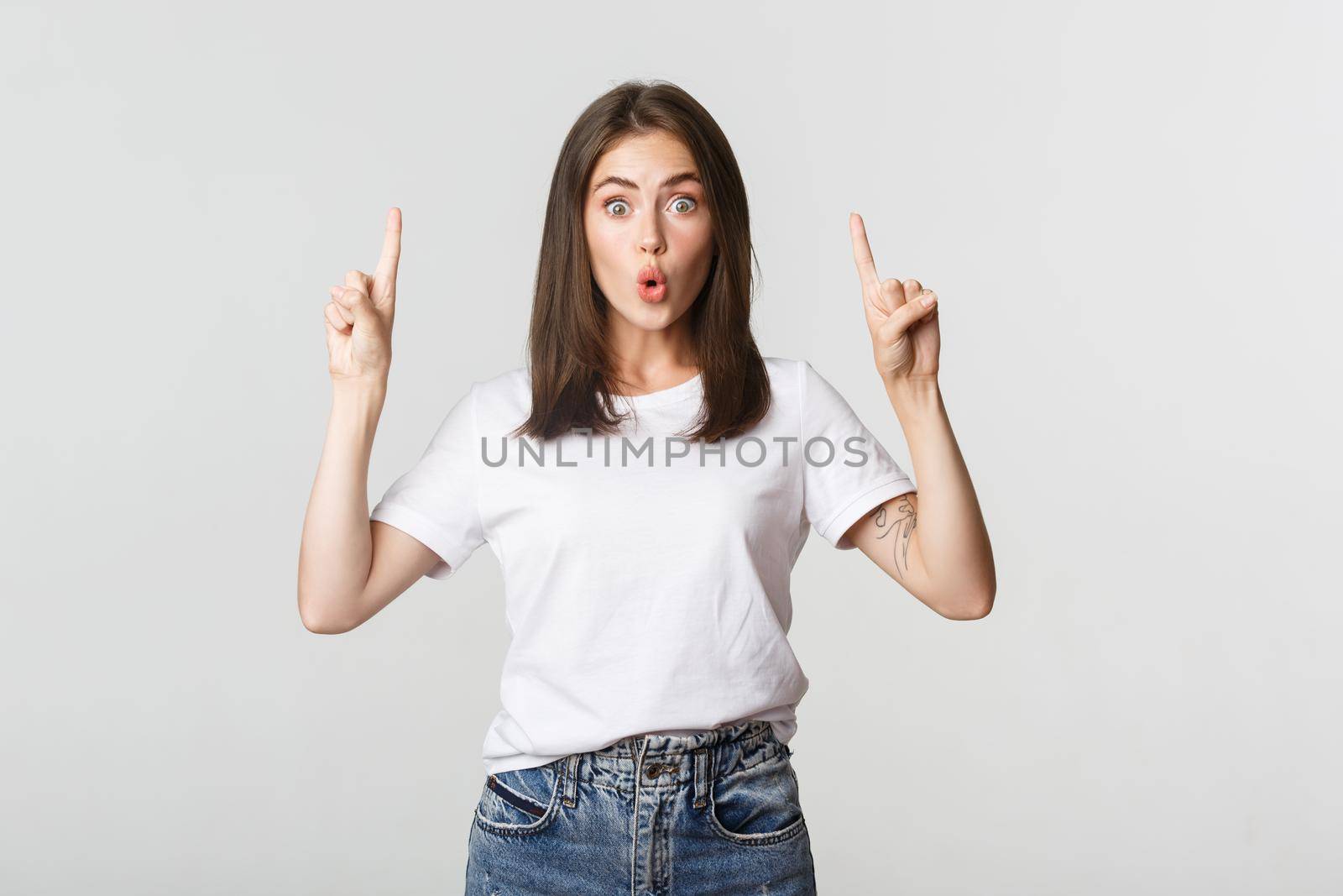 Surprised and impressed brunette girl looking amazed and pointing fingers up by Benzoix